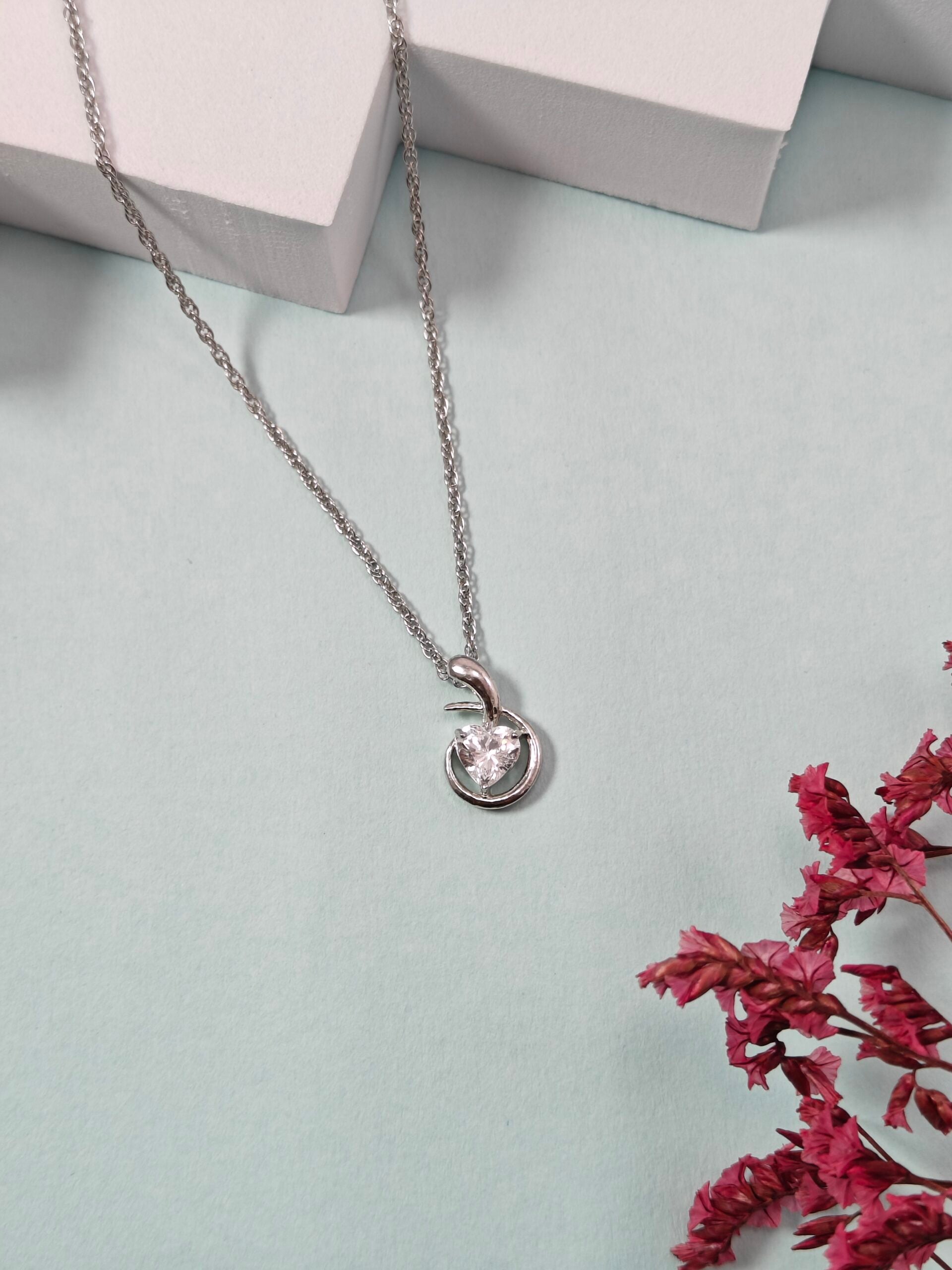 Silver necklace with a pendant on a light gray surface with pink dried flowers.