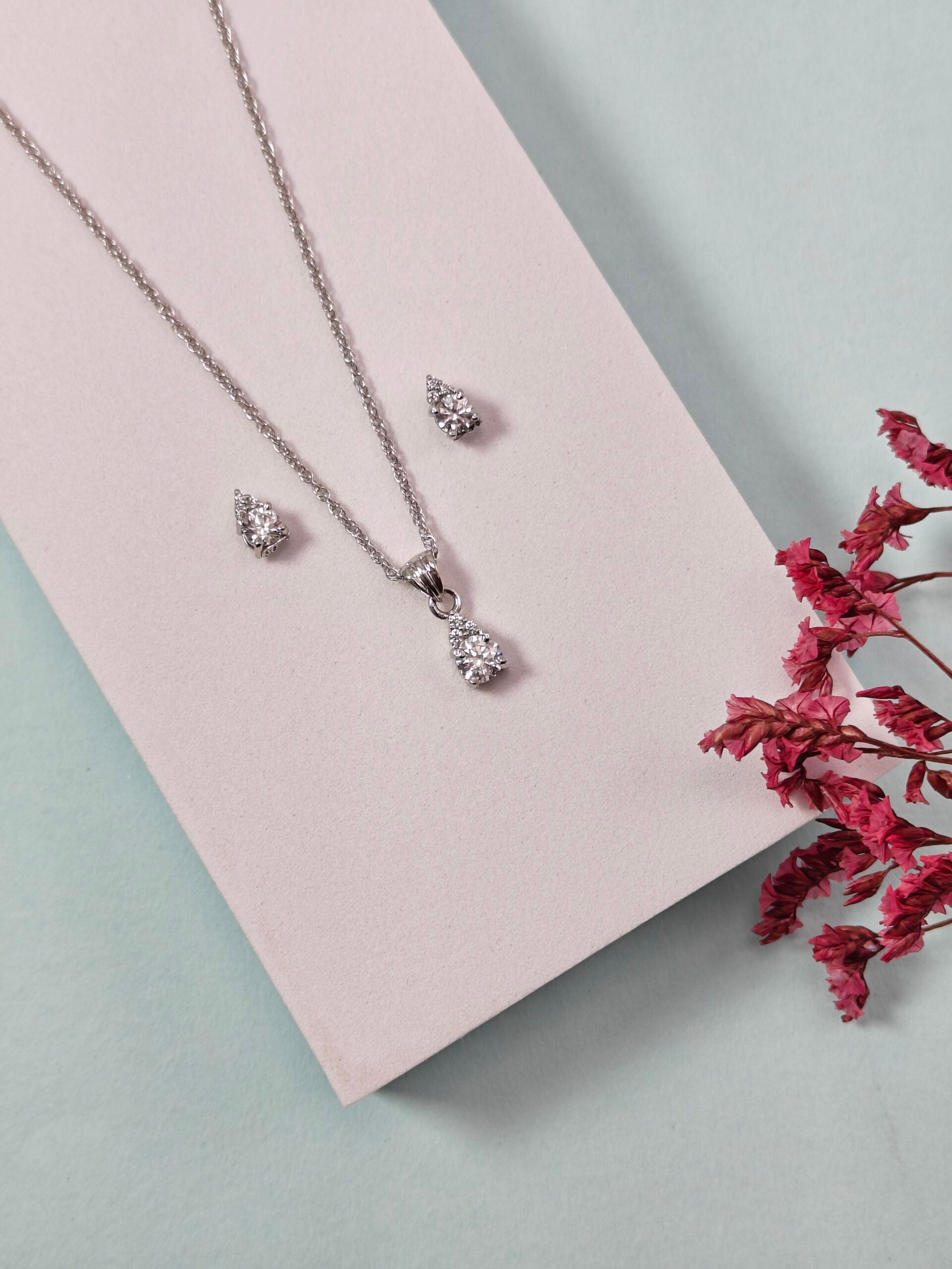 Silver jewelry set with necklace and earrings on a pink card with dried red flowers.