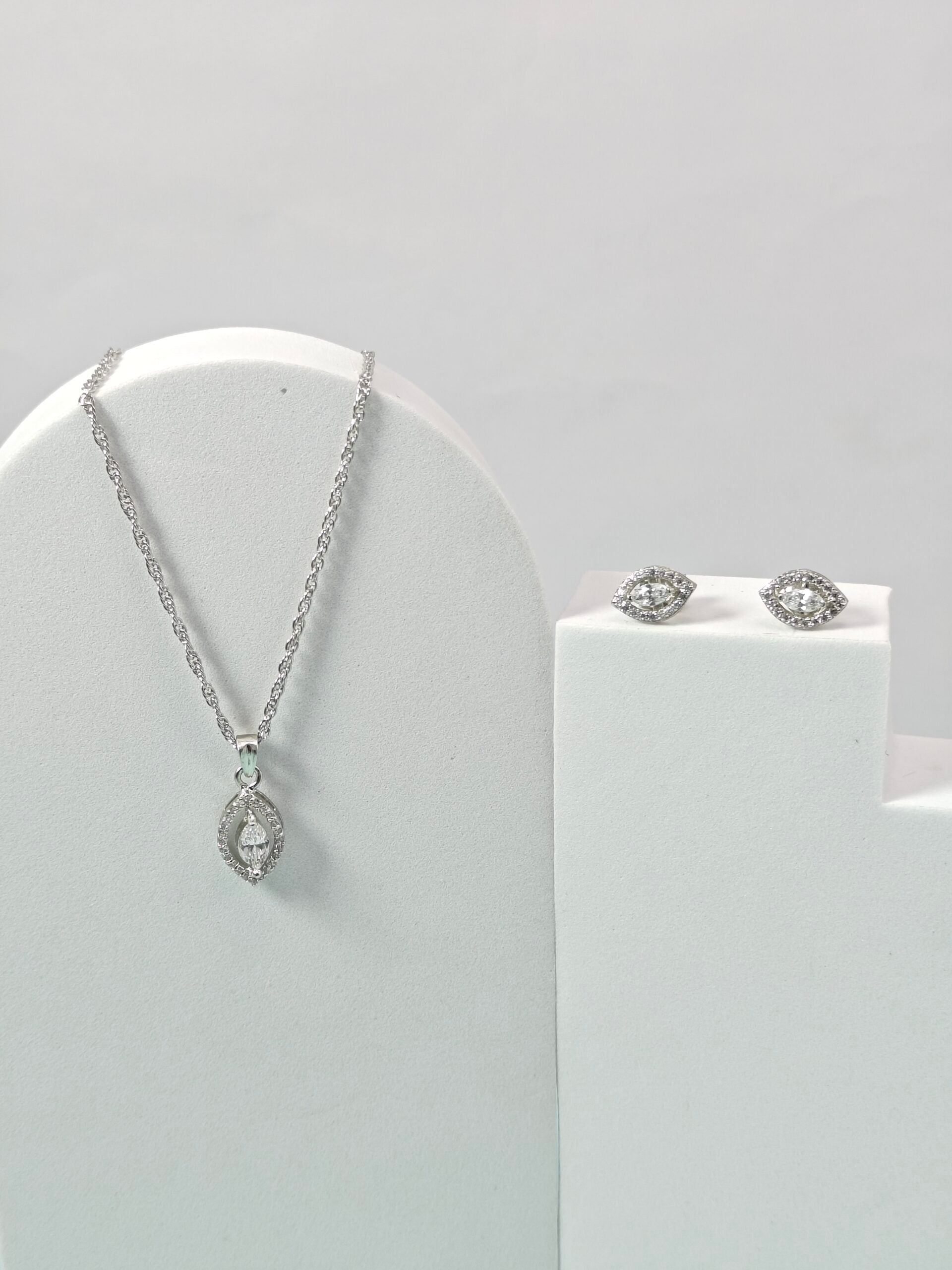 Silver necklace and earrings on a white stand against a light gray background