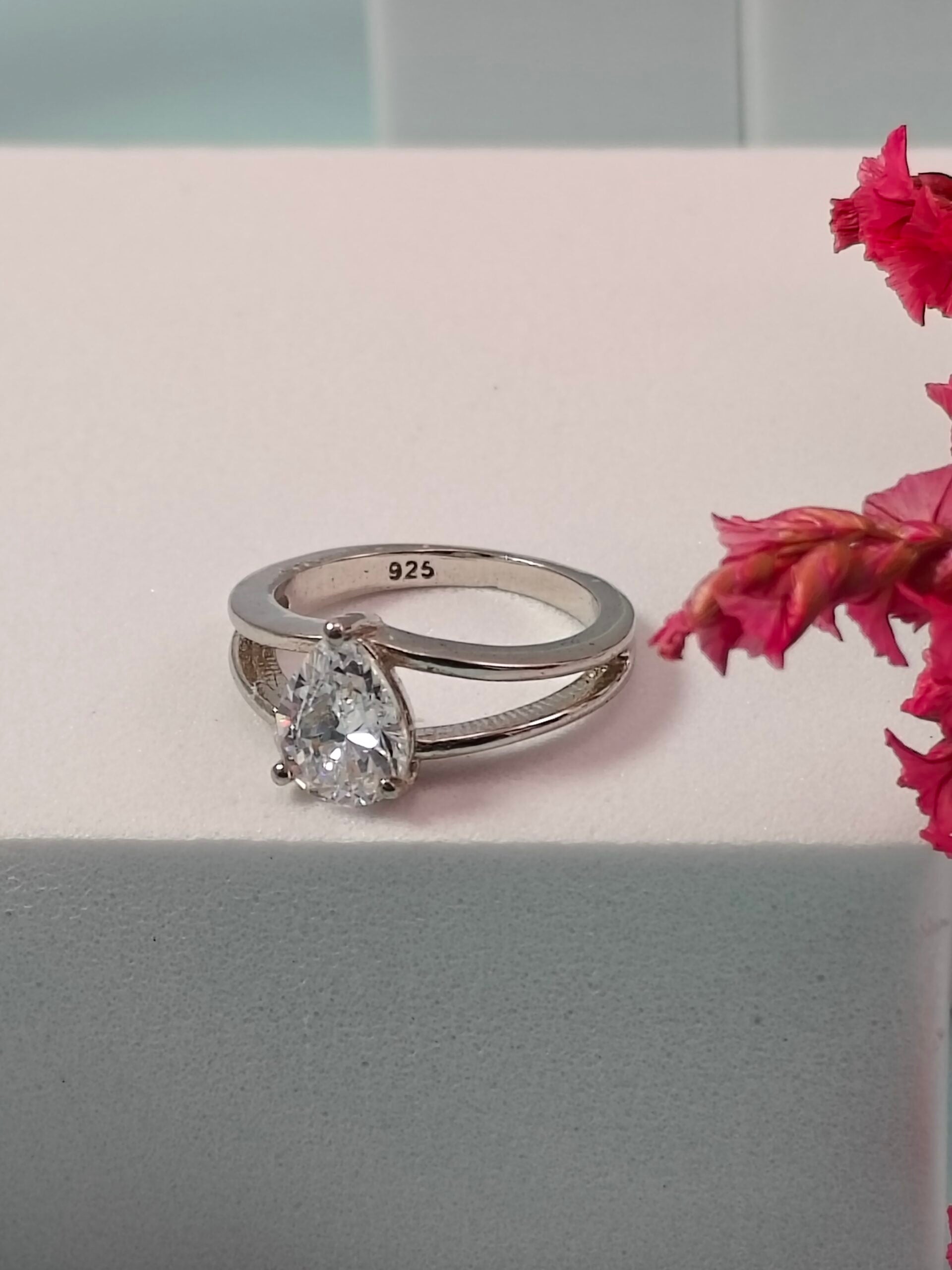 Silver ring with a large diamond on a light pink surface with pink flowers.