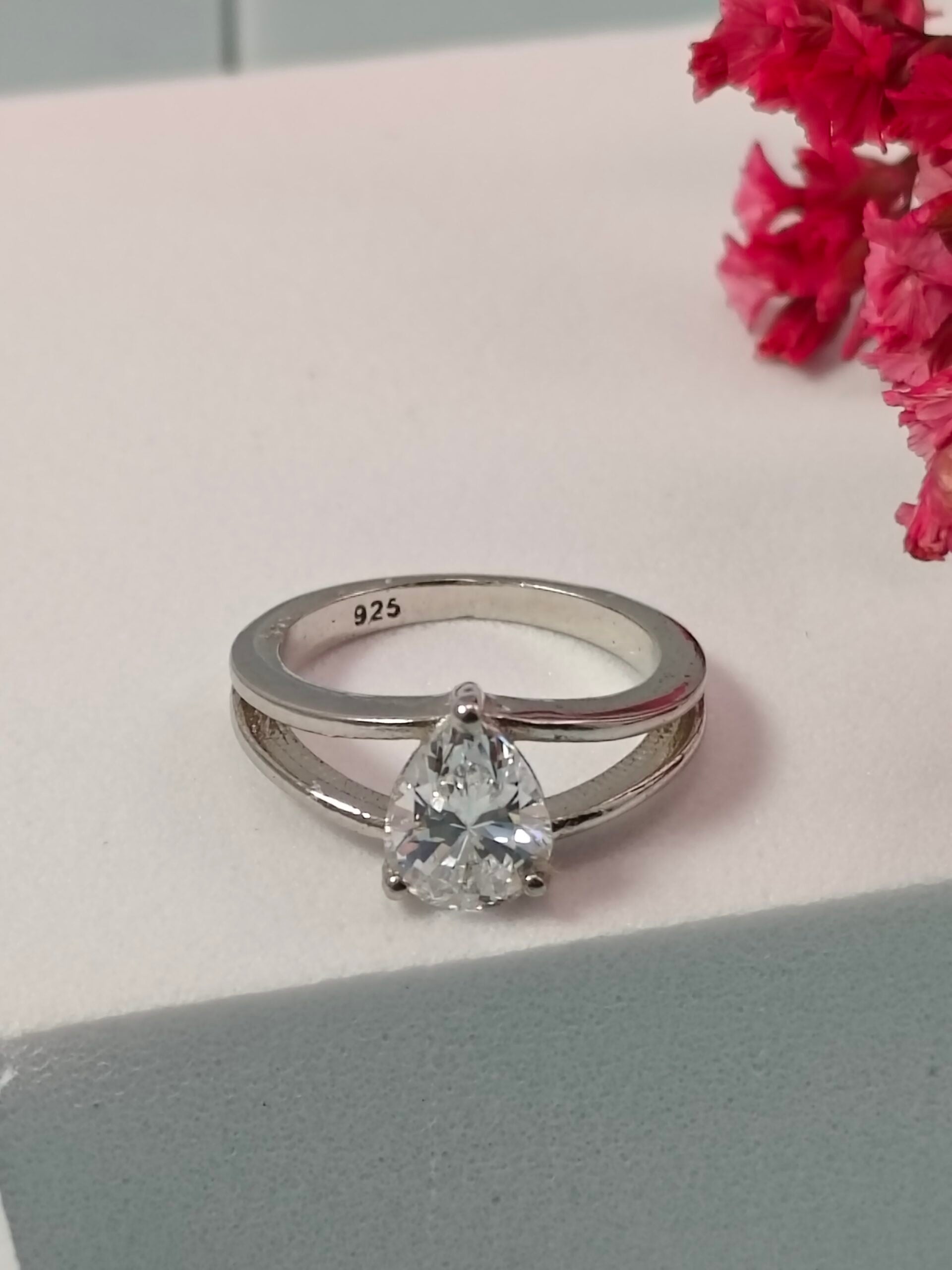 Silver ring with a pear-shaped diamond on a light surface with pink flowers.
