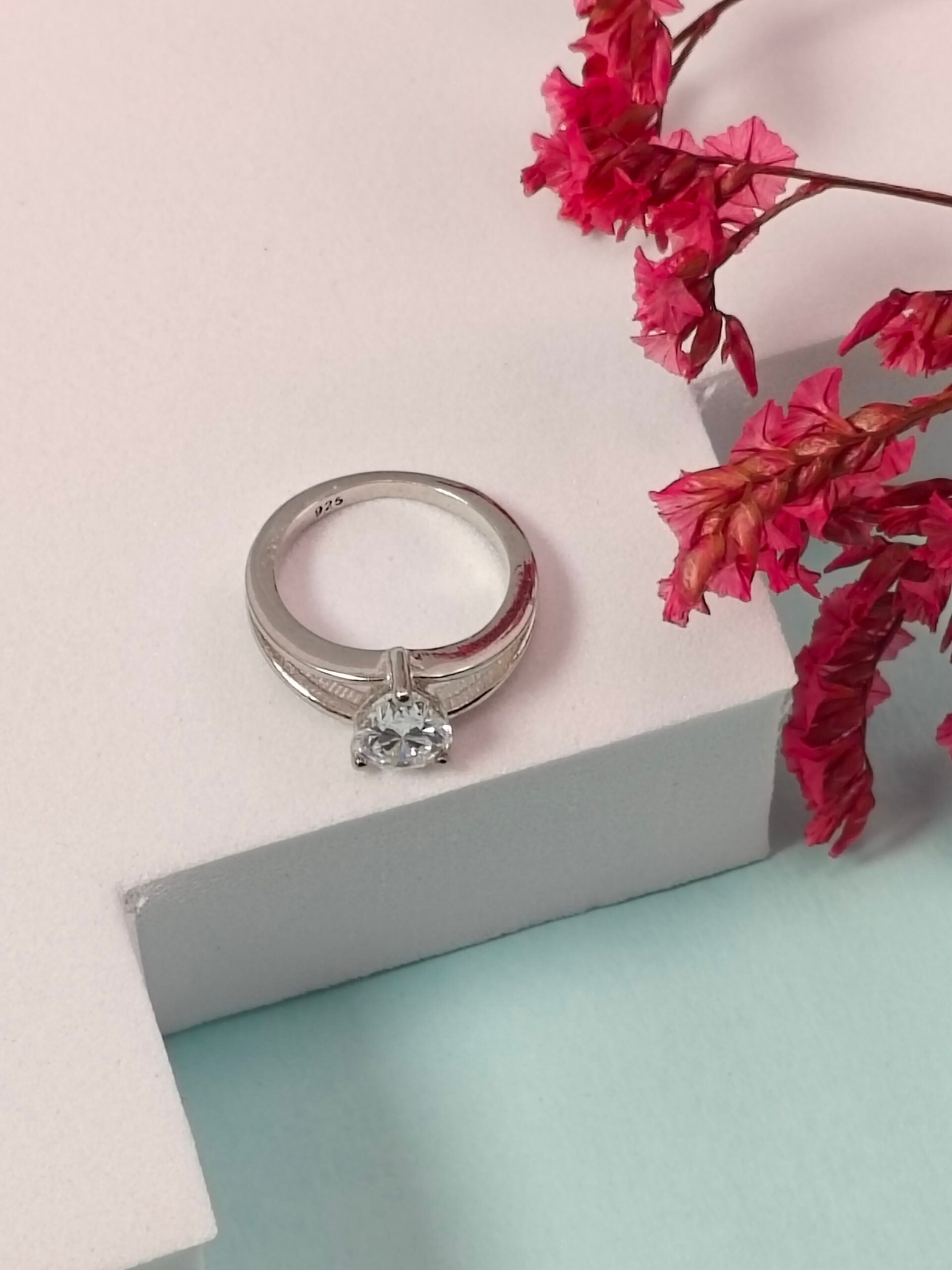 Silver ring with a diamond on a light pink surface with red flowers.
