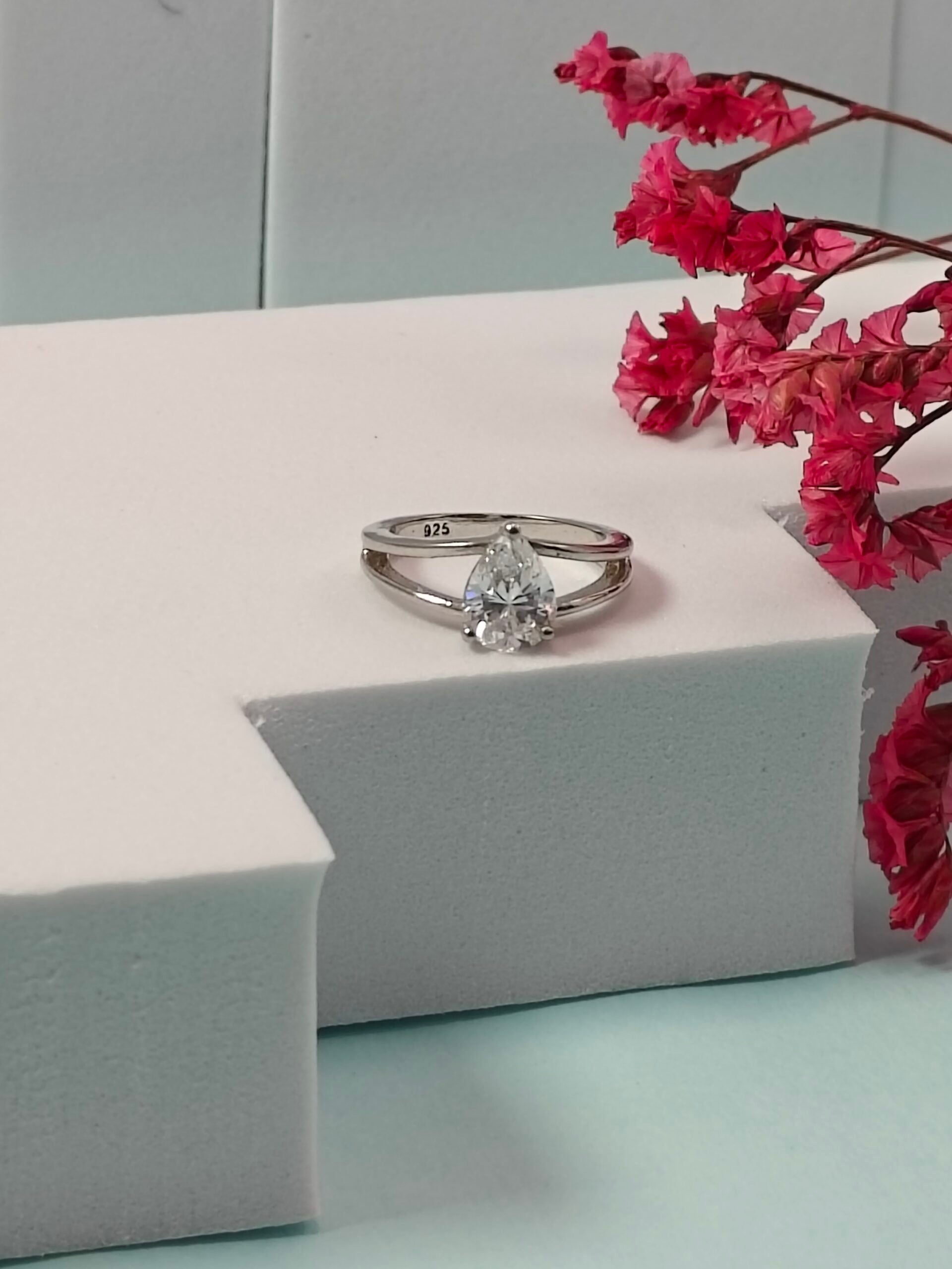 Diamond ring on a white surface with pink flowers in the background