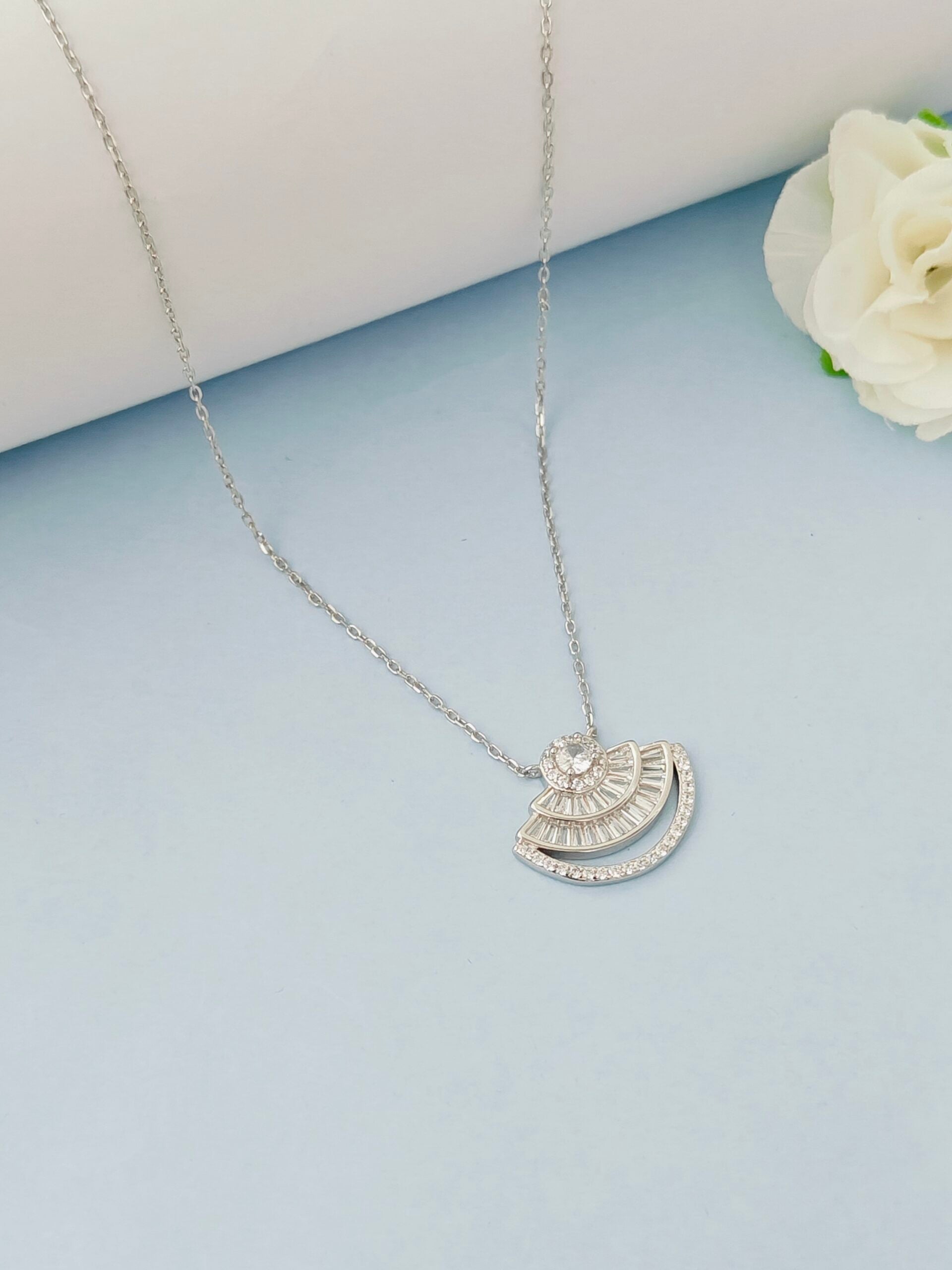Silver necklace with a half-circle pendant on a light blue surface with a white flower.