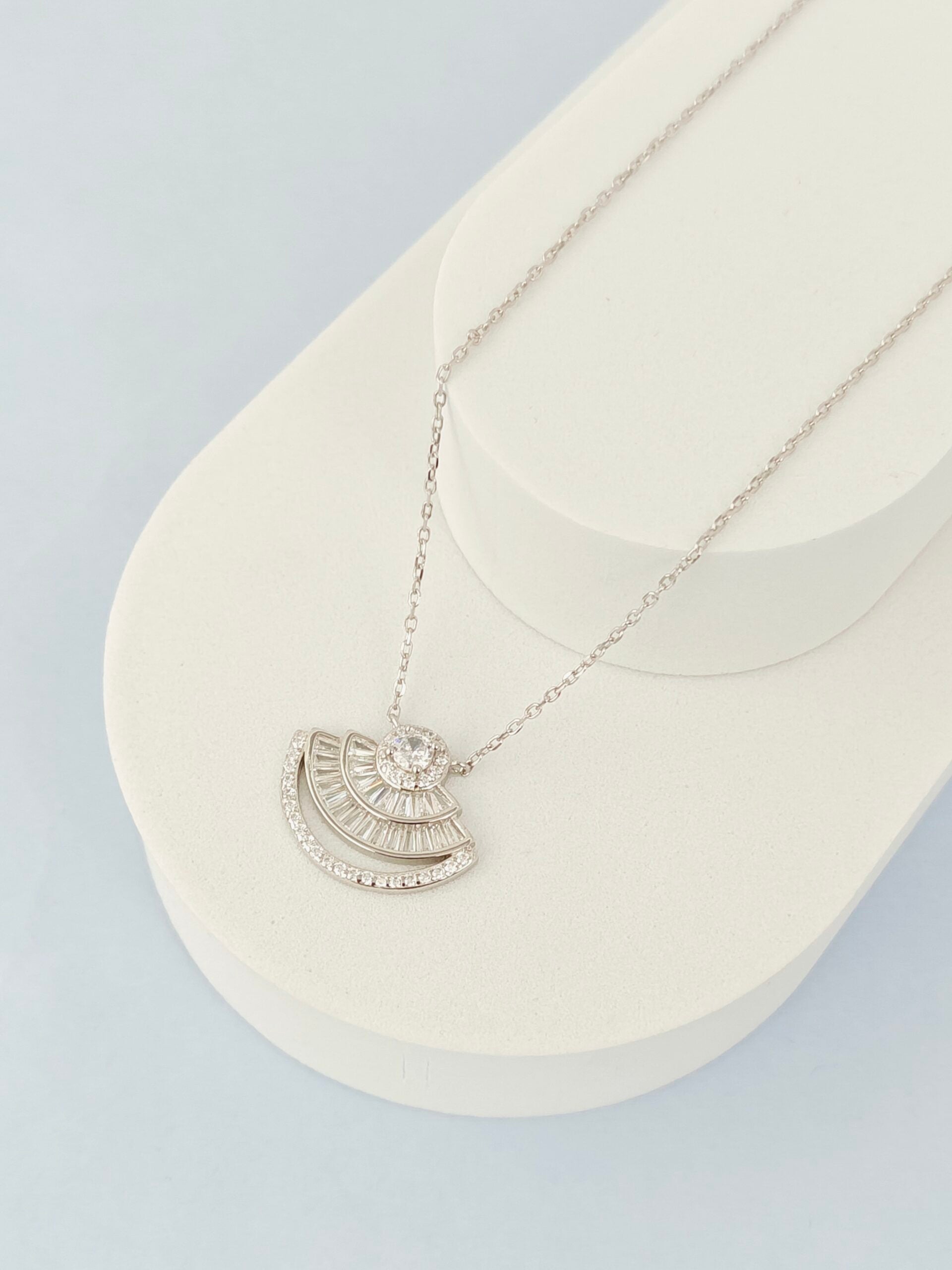 Silver necklace with a half-circle pendant on a white cushion against a light gray background