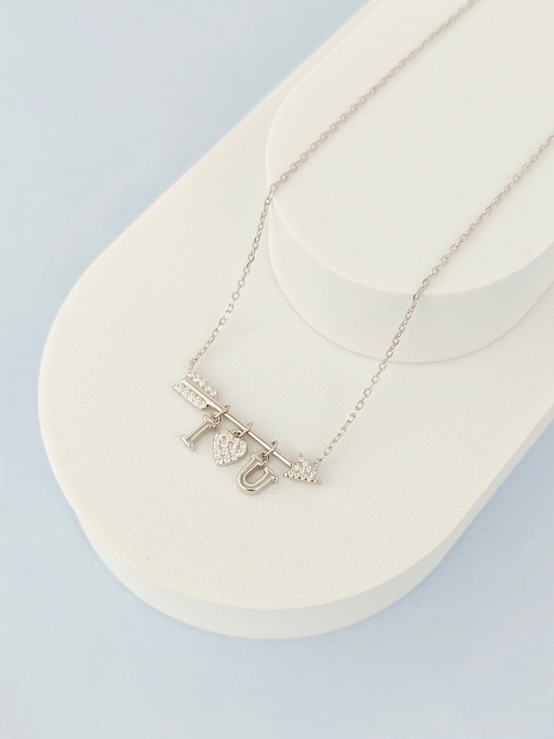 Silver necklace with 'I love you' pendant on a white stand against a light gray background