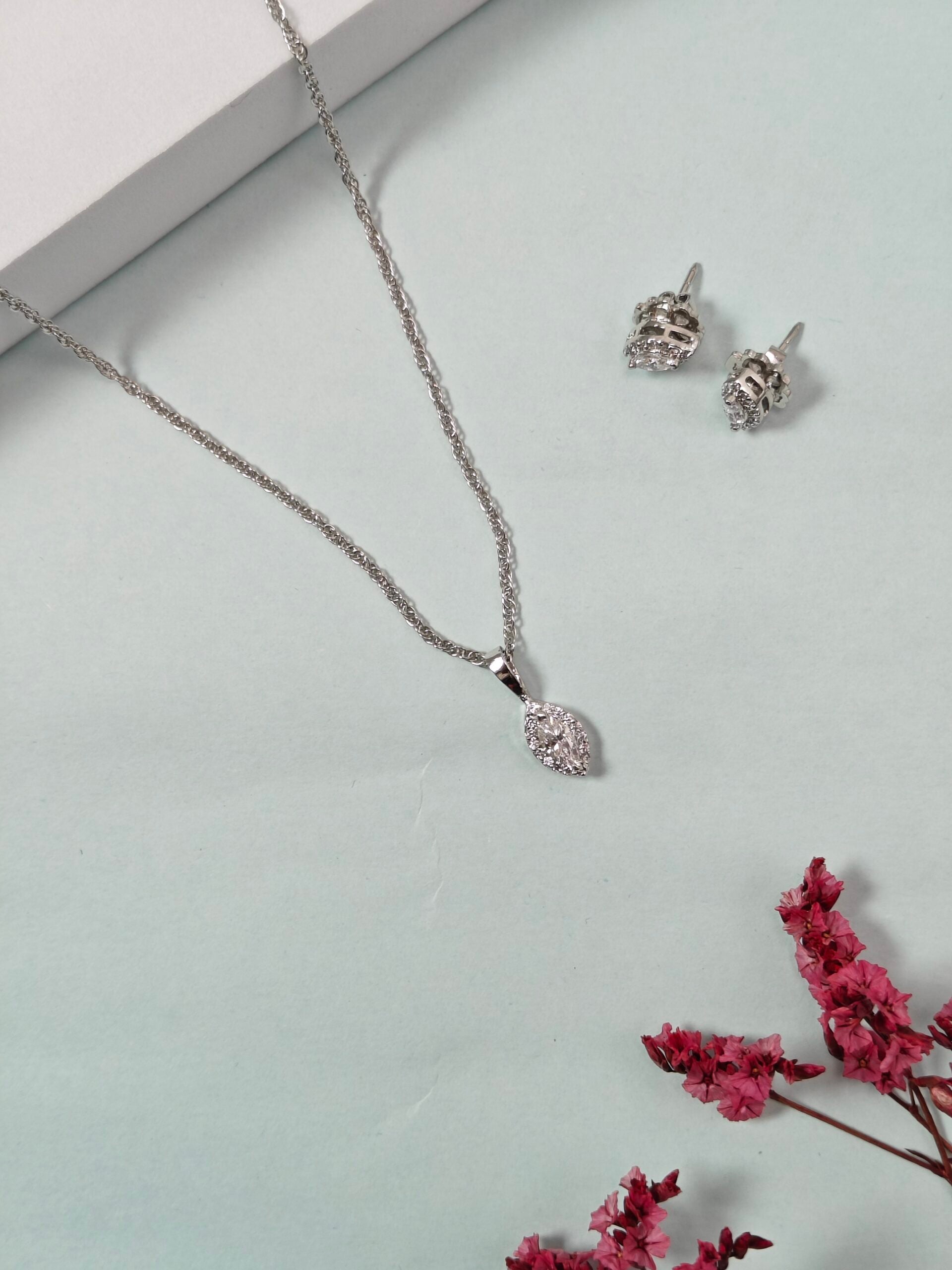 Silver necklace and earrings with pink flowers on a light gray background