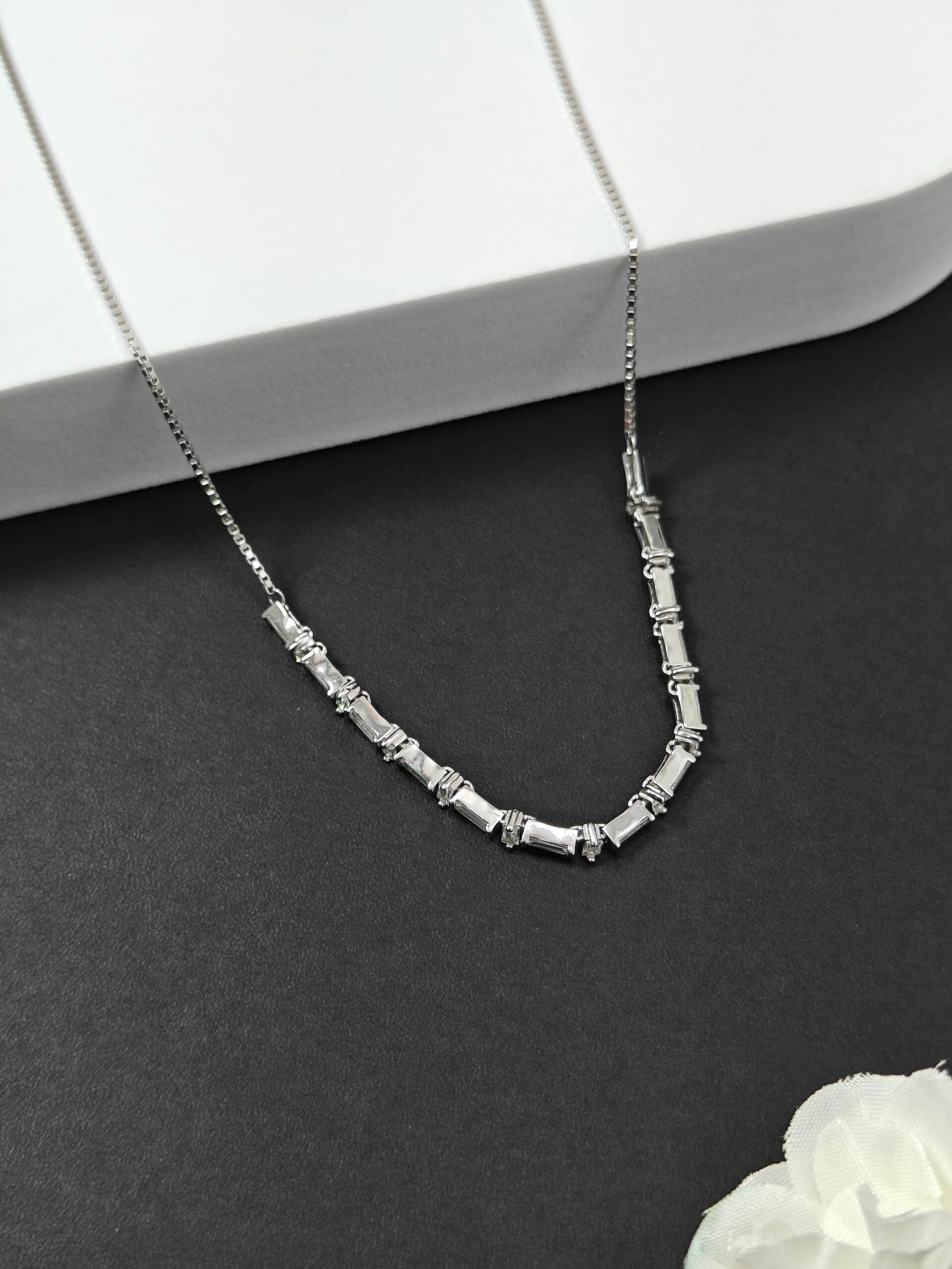 Silver beaded necklace on a dark surface with a white object in the corner