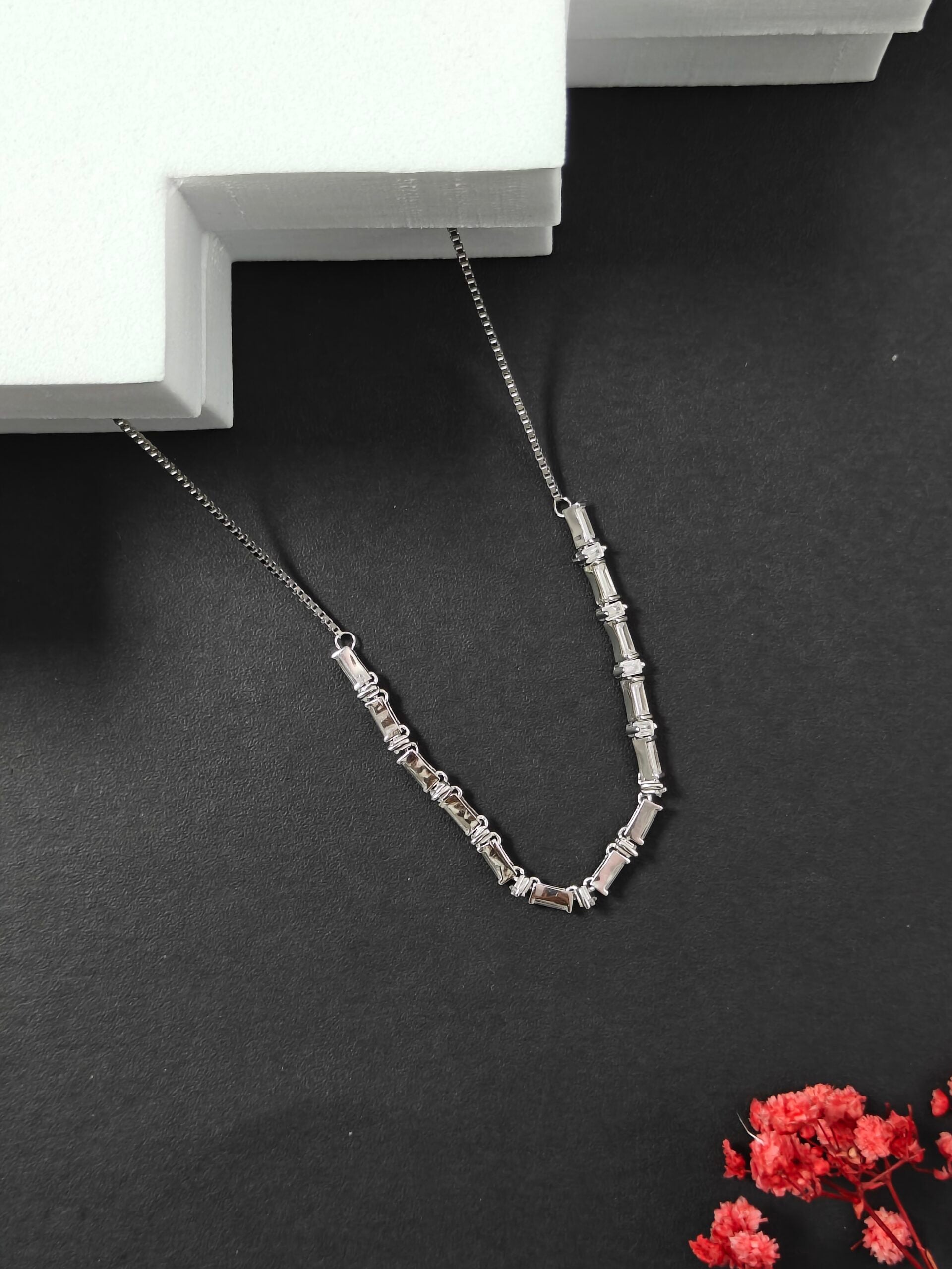 Silver necklace on a dark surface with a white box in the background