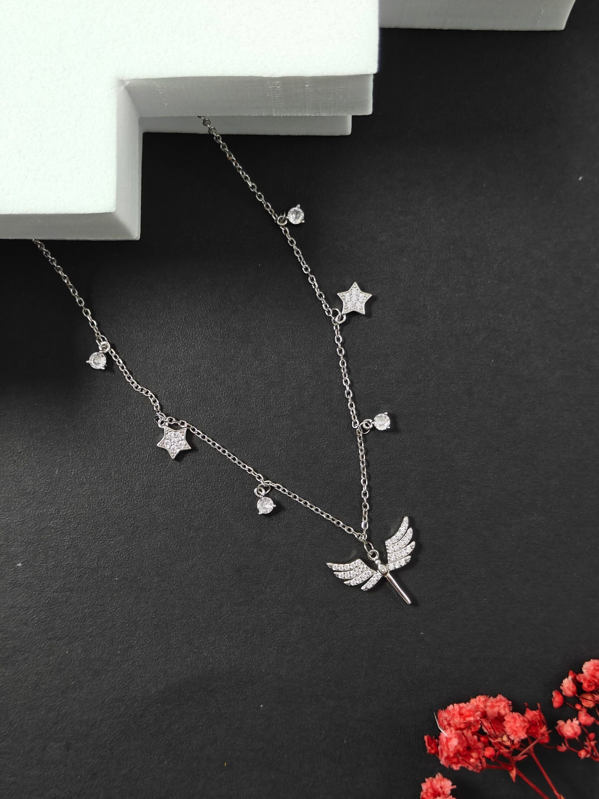Silver necklace with star and leaf pendants on a dark surface with red flowers.