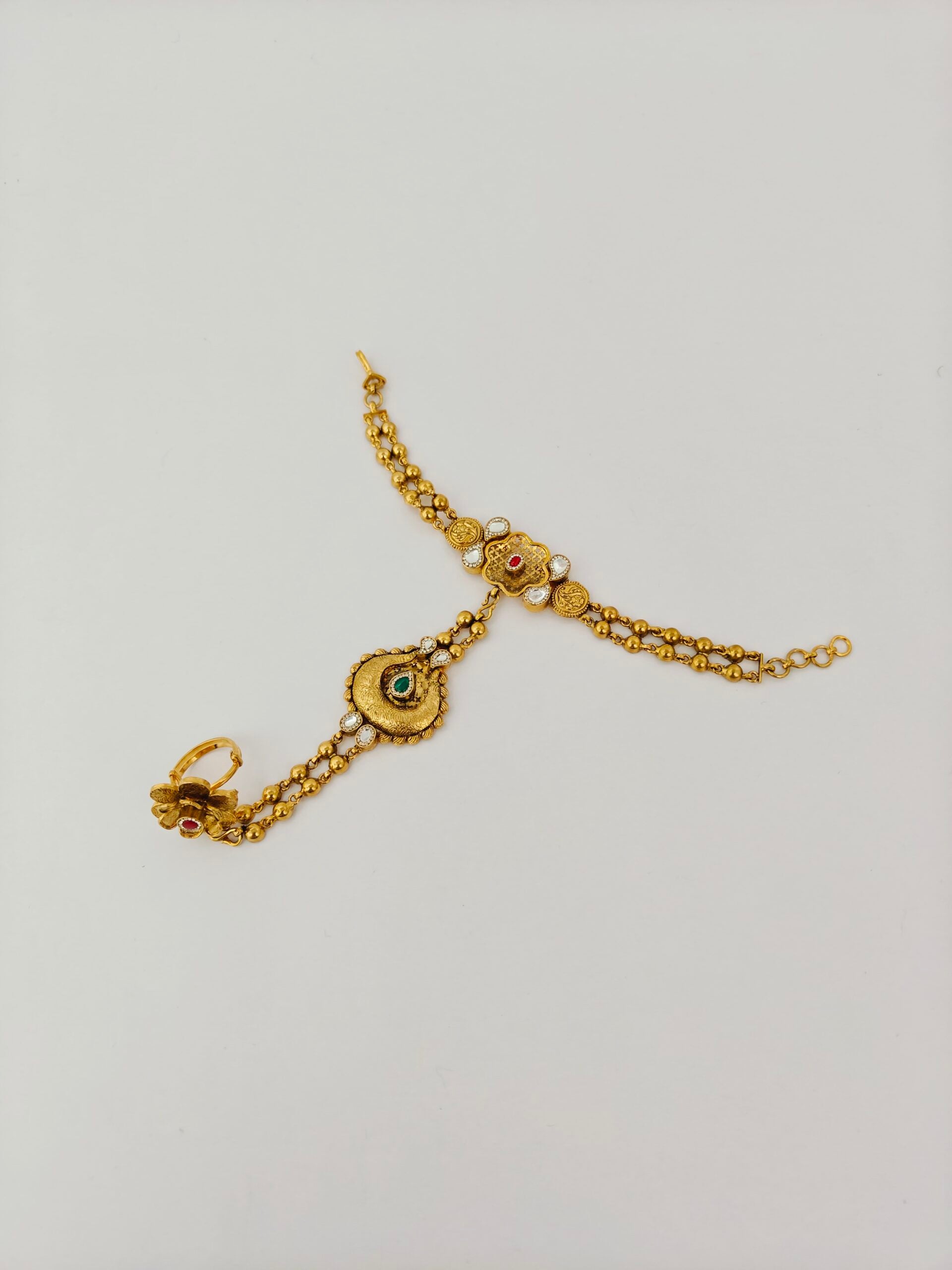 Gold bracelet with emerald and diamond accents on a light gray background