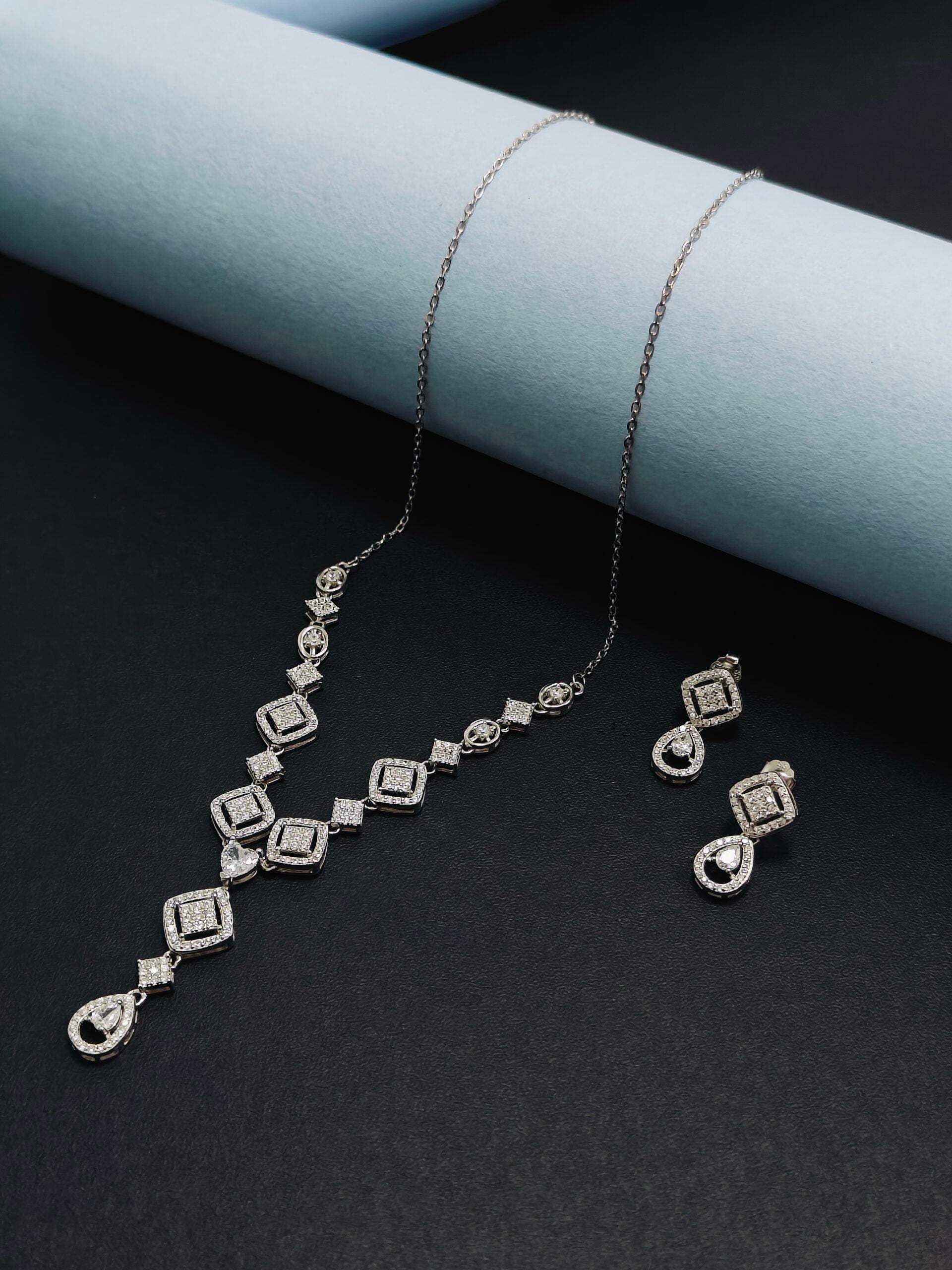 Silver necklace and earrings set on a dark surface with light blue background