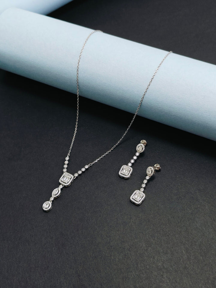 Silver necklace and earrings set on a dark surface with a light blue cylindrical object.