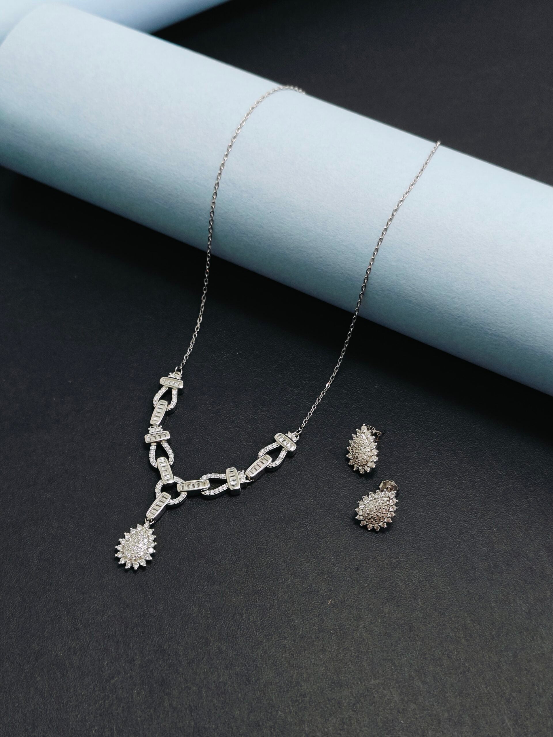 Silver necklace and earrings on a dark surface with light blue paper