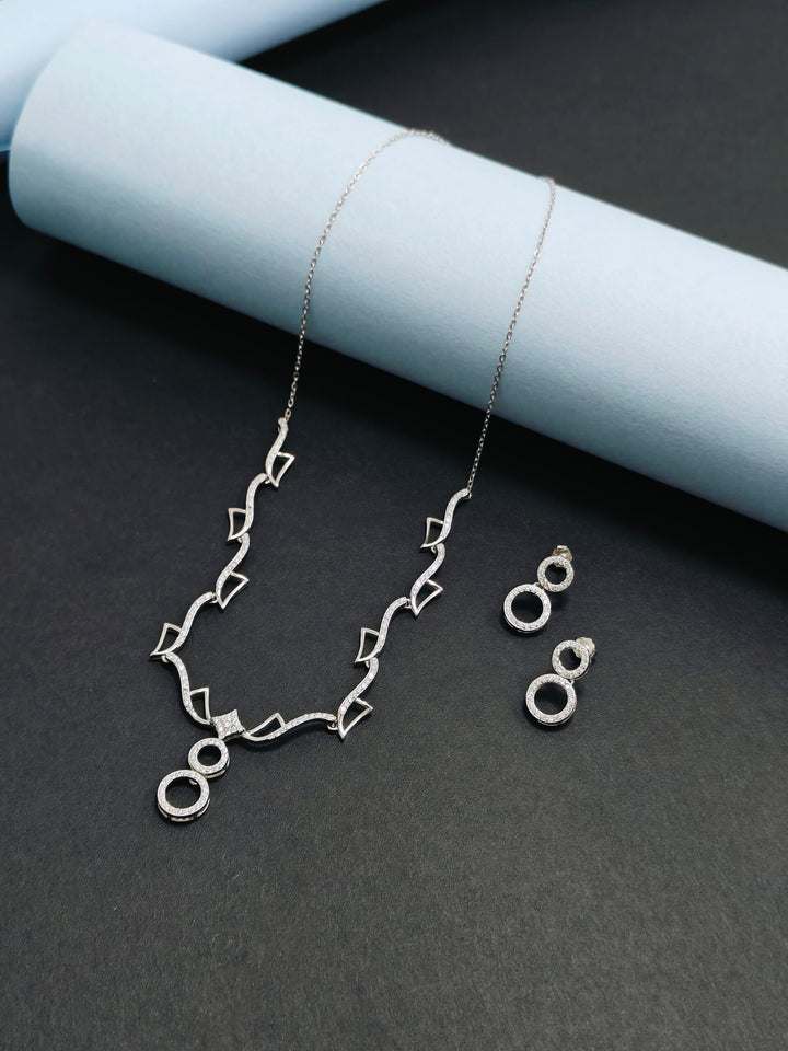 Silver necklace and earrings on a dark surface with light blue cylindrical objects.