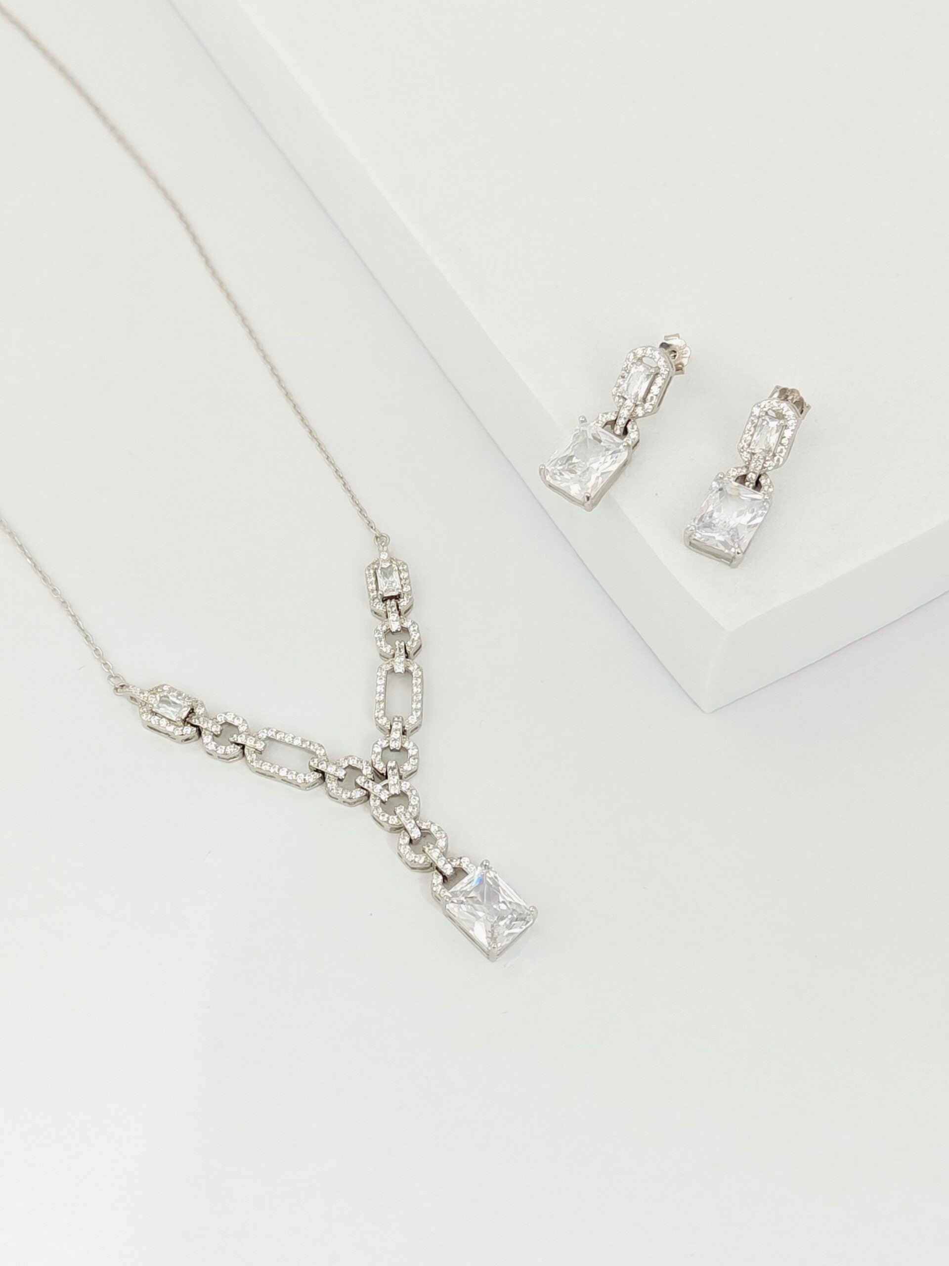 Silver necklace and earrings on a light gray background