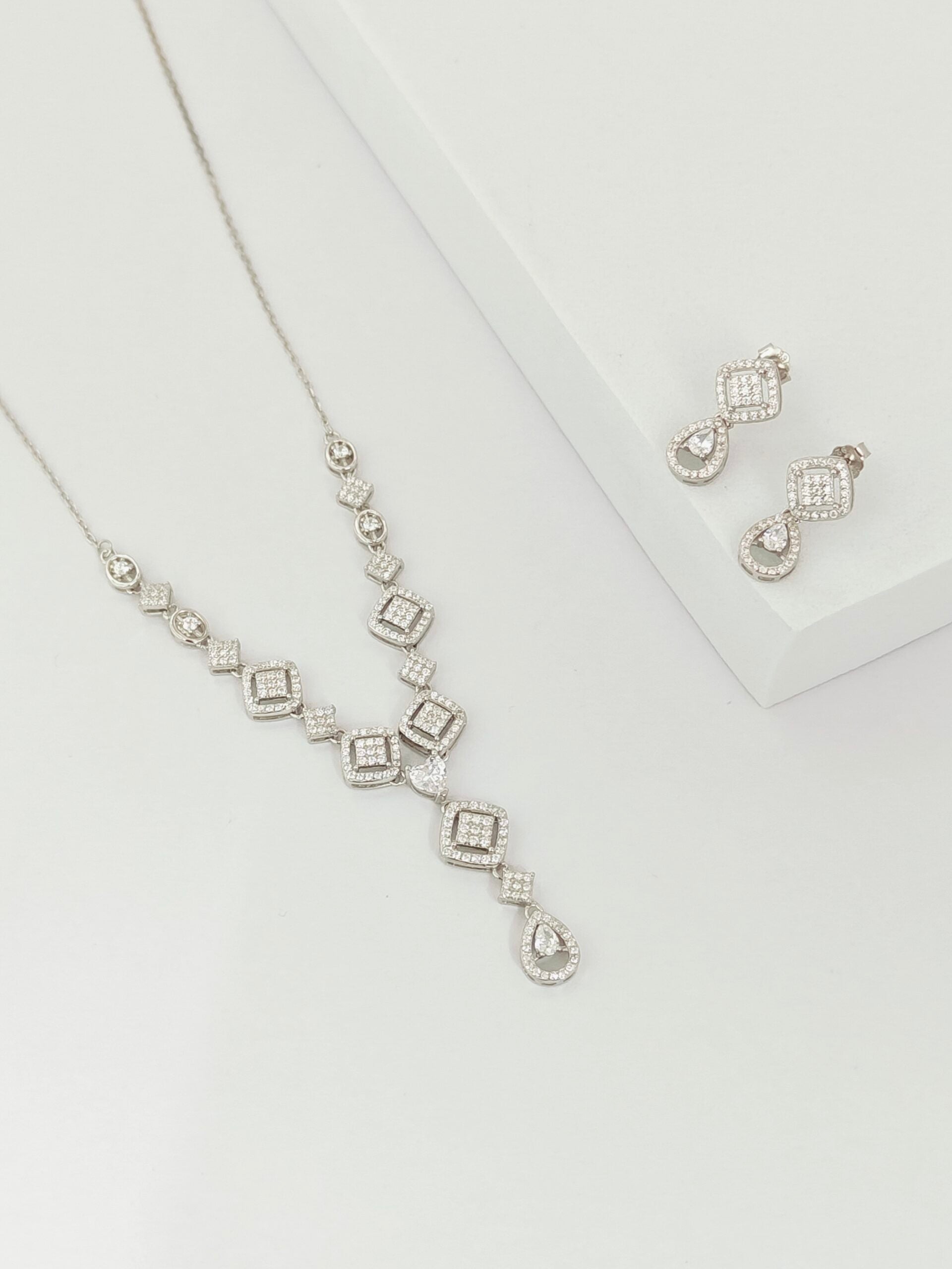 Silver necklace and earrings on a light gray background