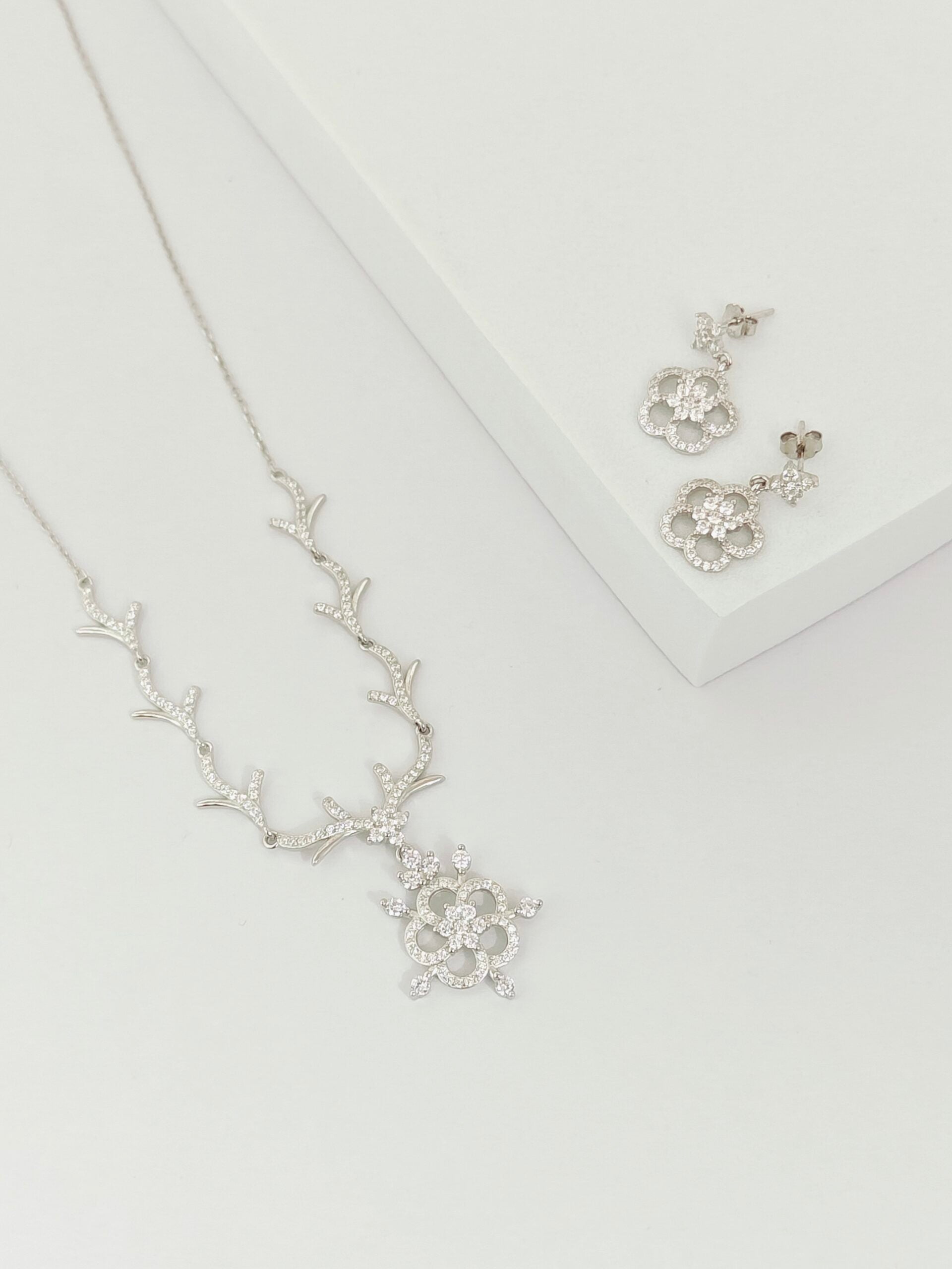 Silver necklace and earrings set on a light gray background