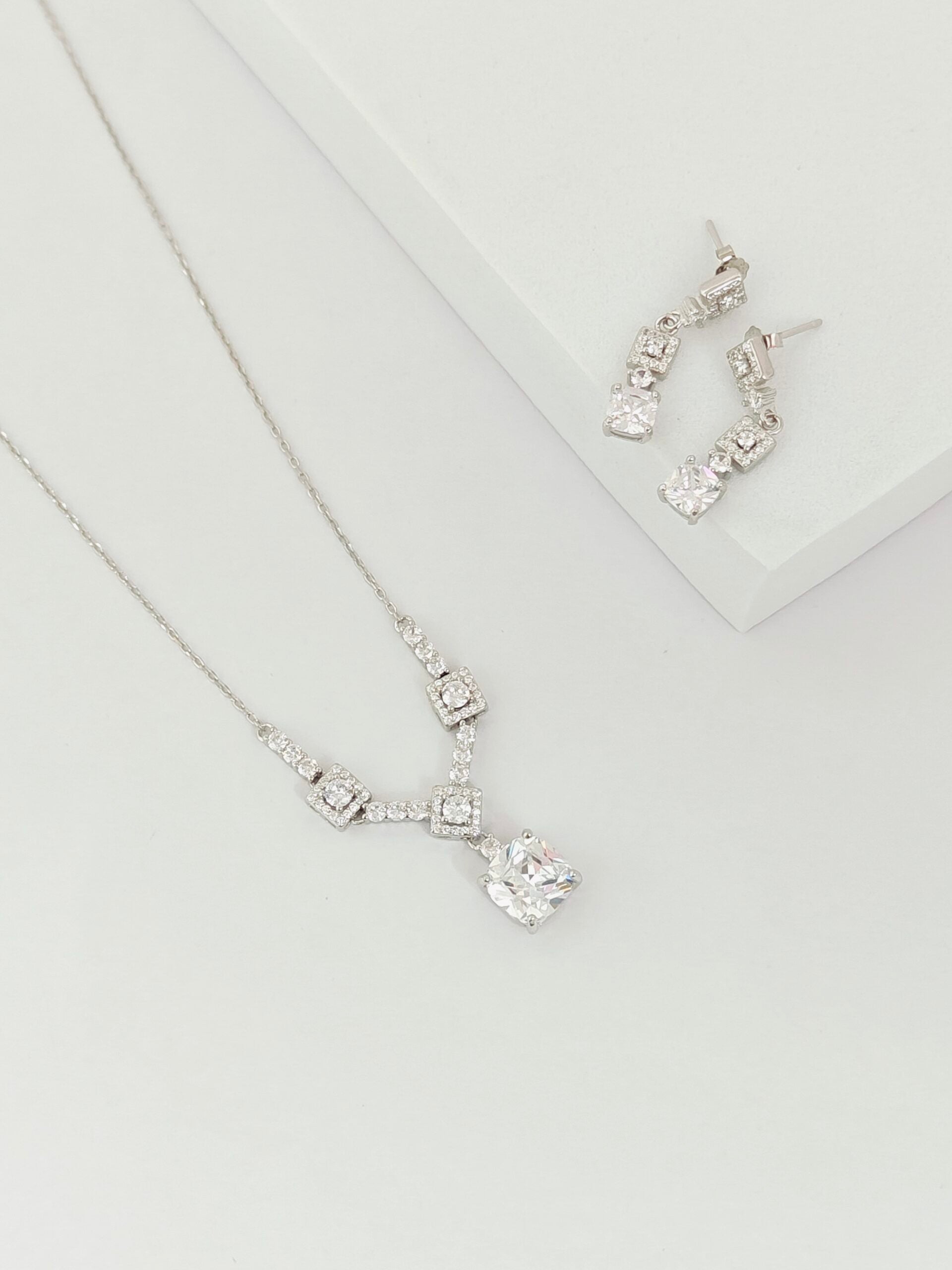 Silver necklace and earrings on a light gray background