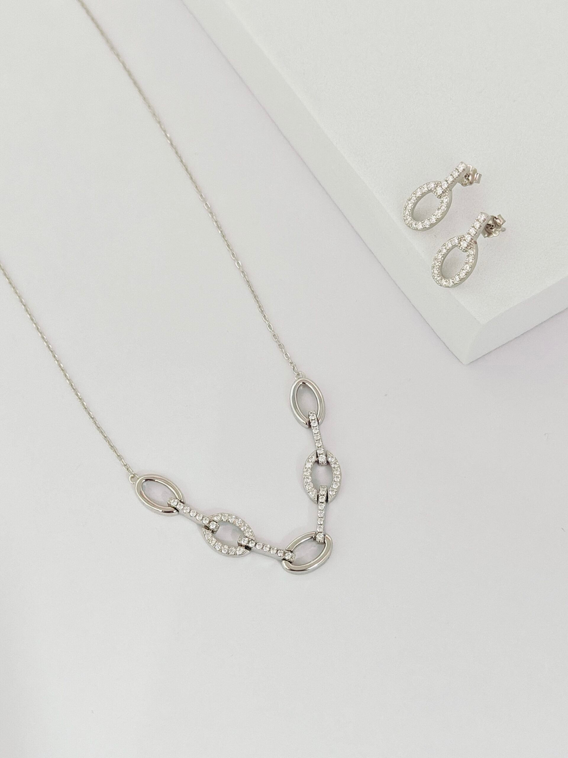 Silver necklace and earrings on a light gray background