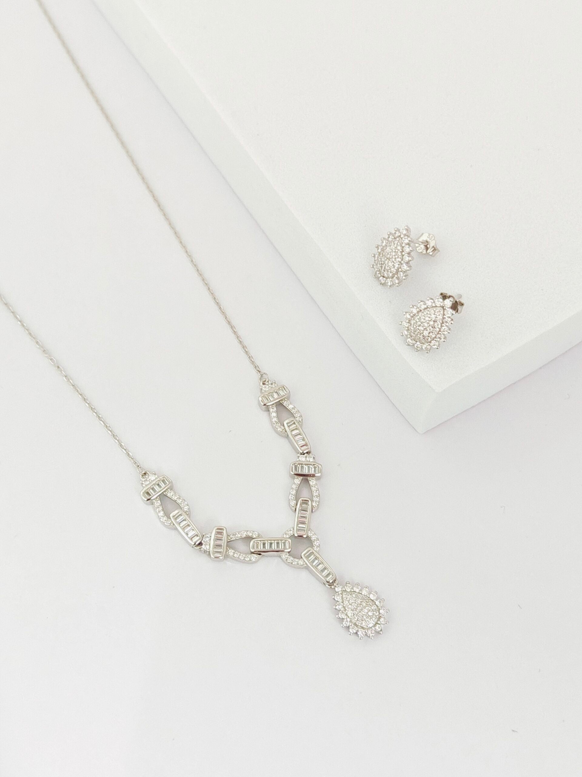 Silver necklace and earrings on a white surface