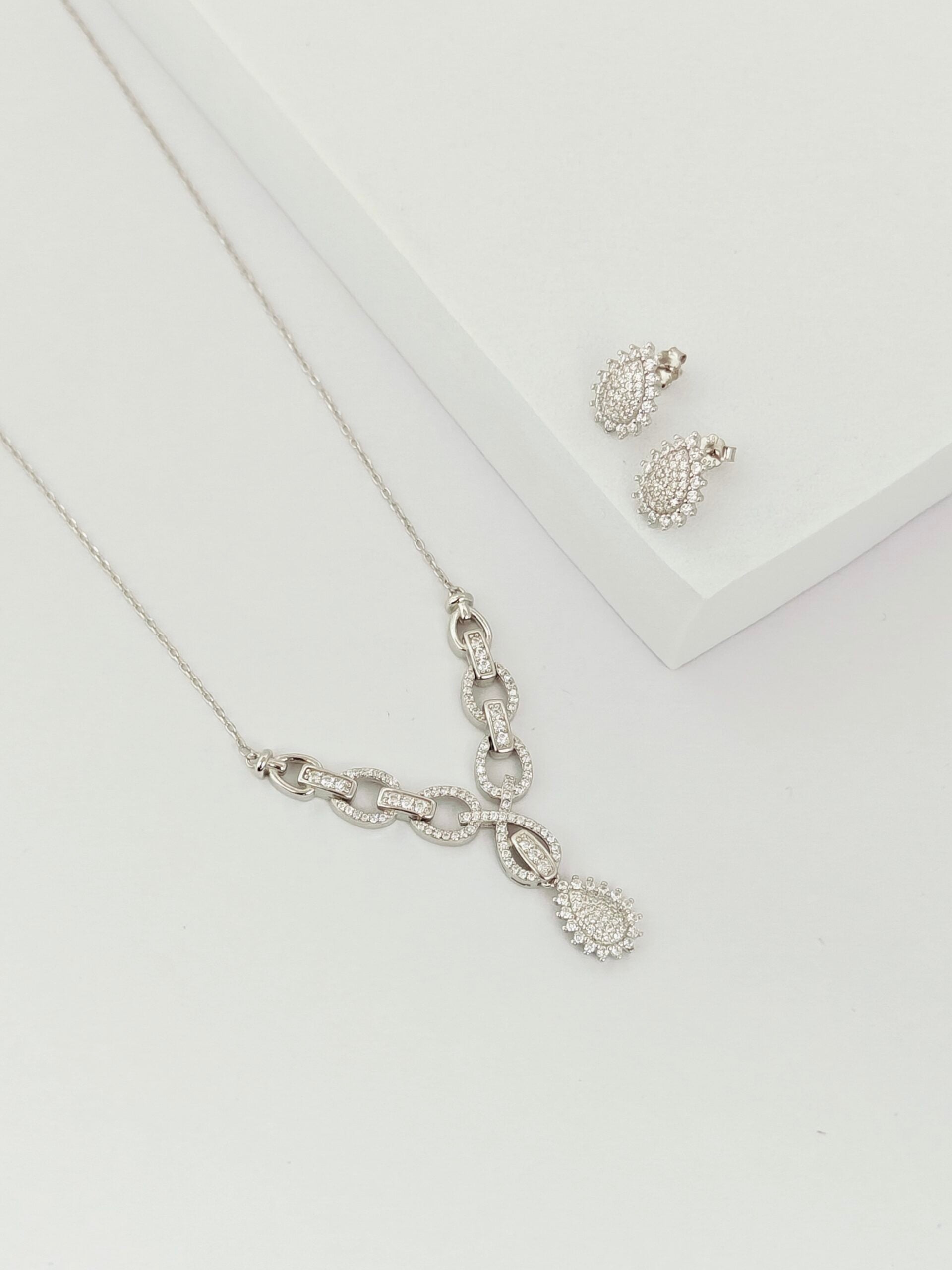 Silver necklace and earrings on a light gray background