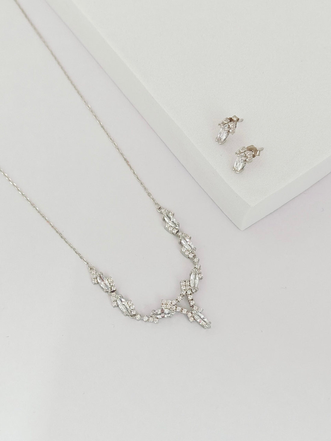Silver necklace and earrings on a light gray background