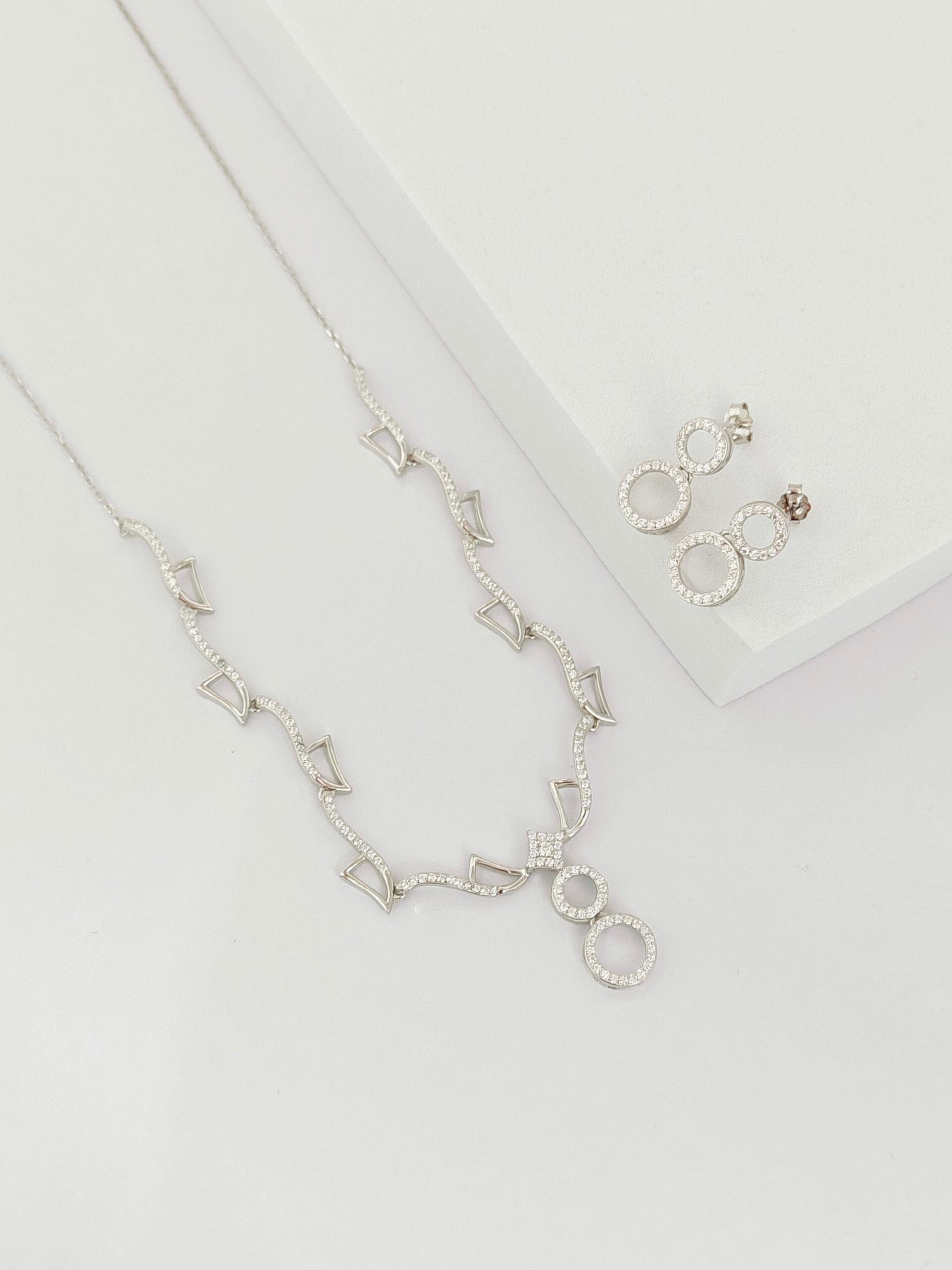 Silver necklace and earrings on a light gray background