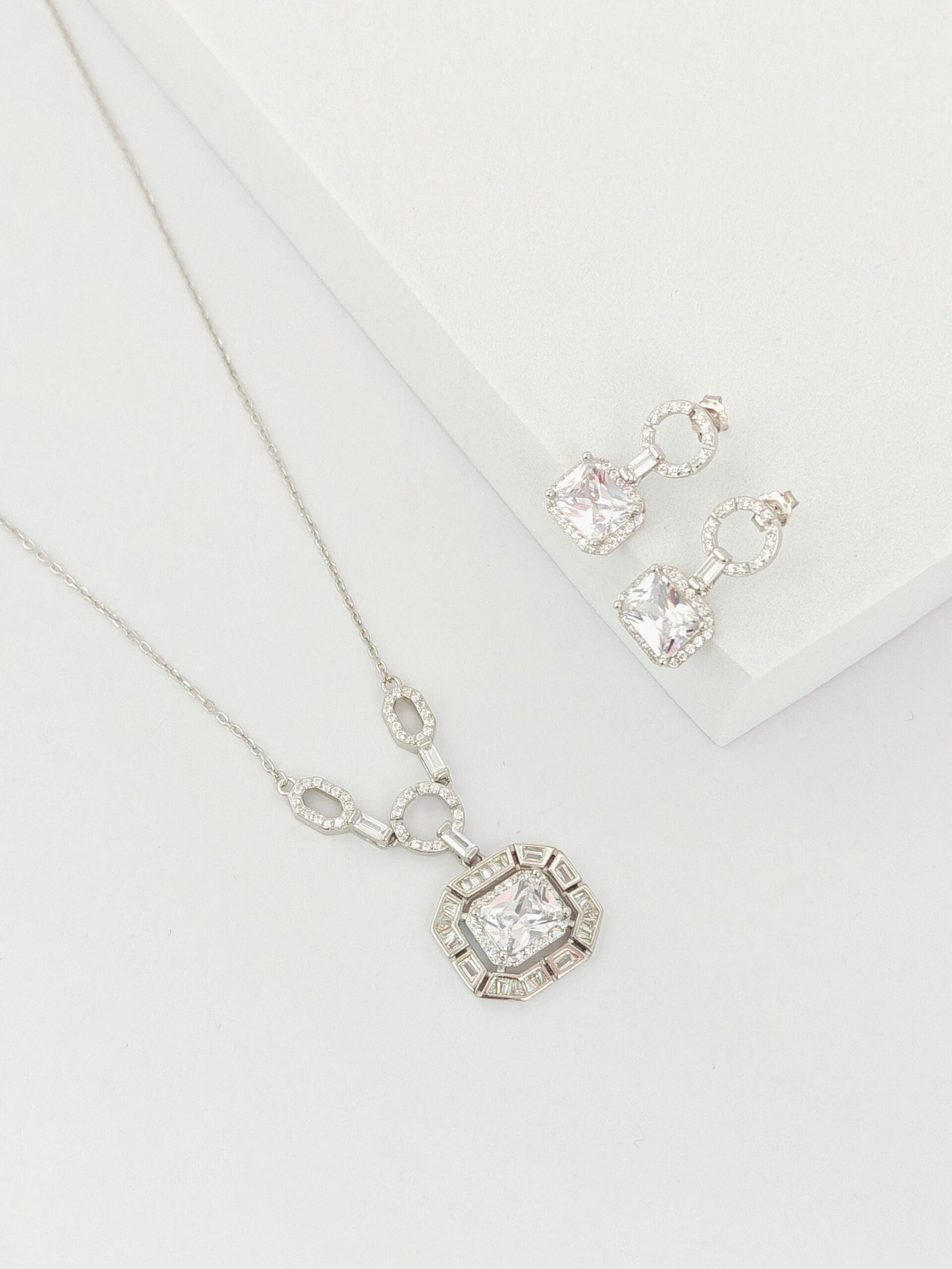Silver necklace and earrings set on a white background