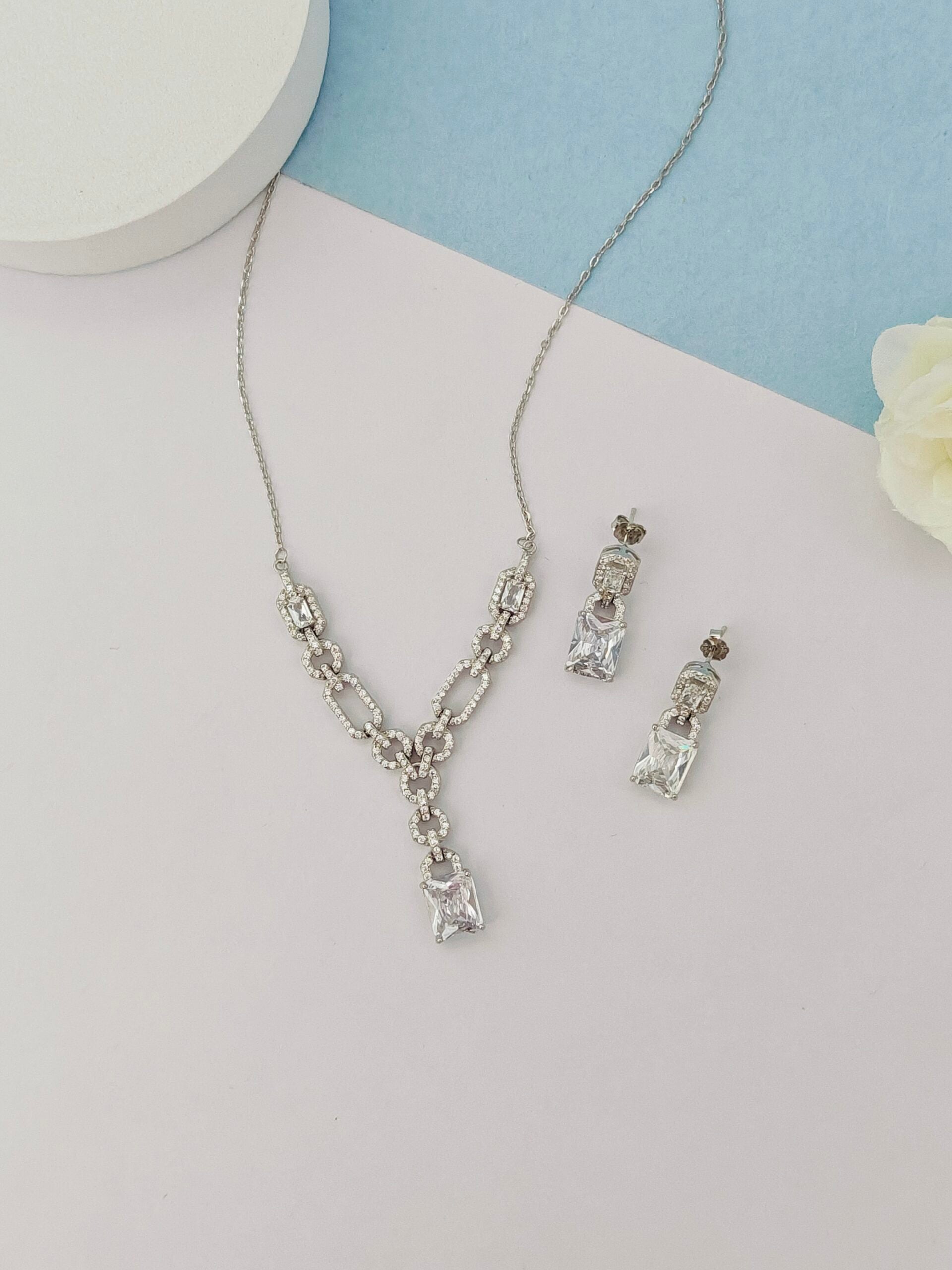 Silver necklace and earrings on a light gray background
