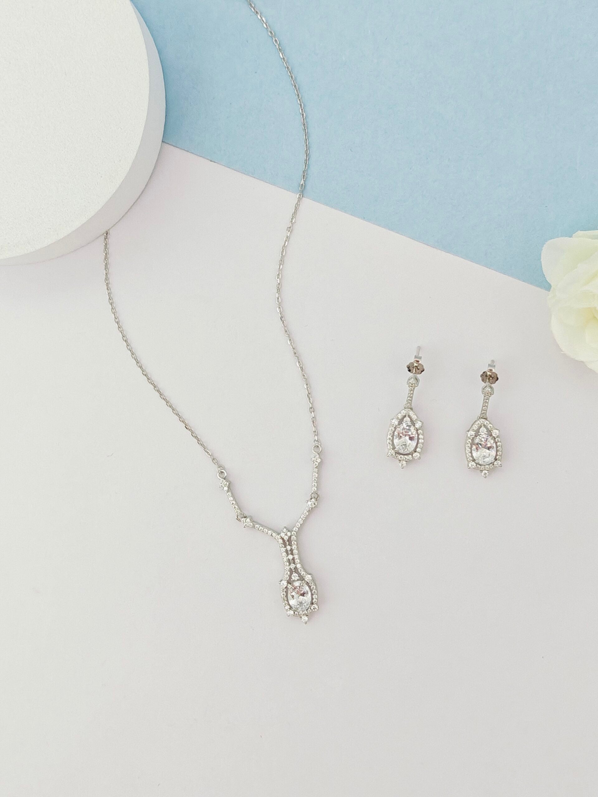 Silver necklace and earrings on a light gray surface with a blue background
