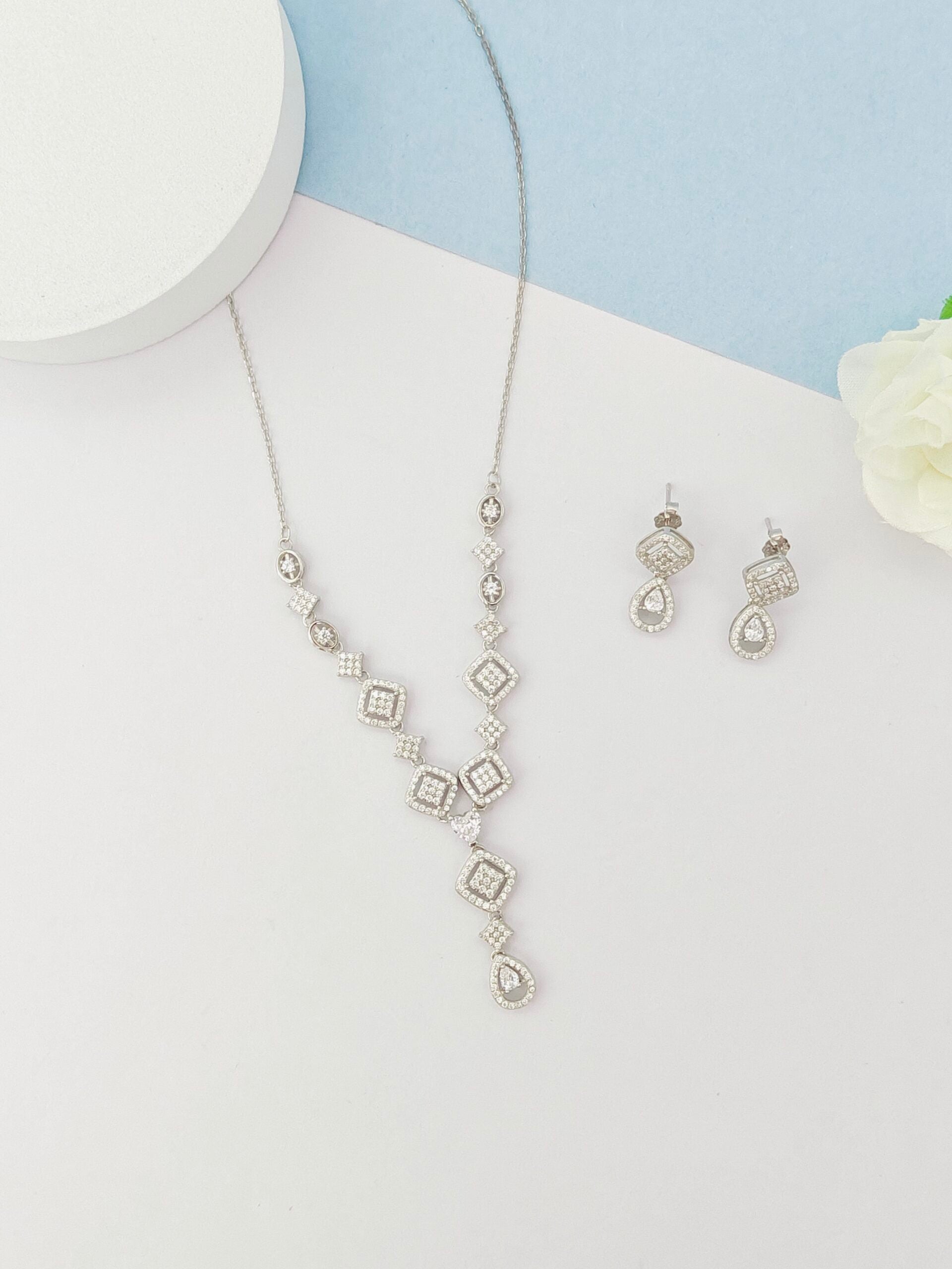 Silver necklace and earrings on a white surface with a light blue background