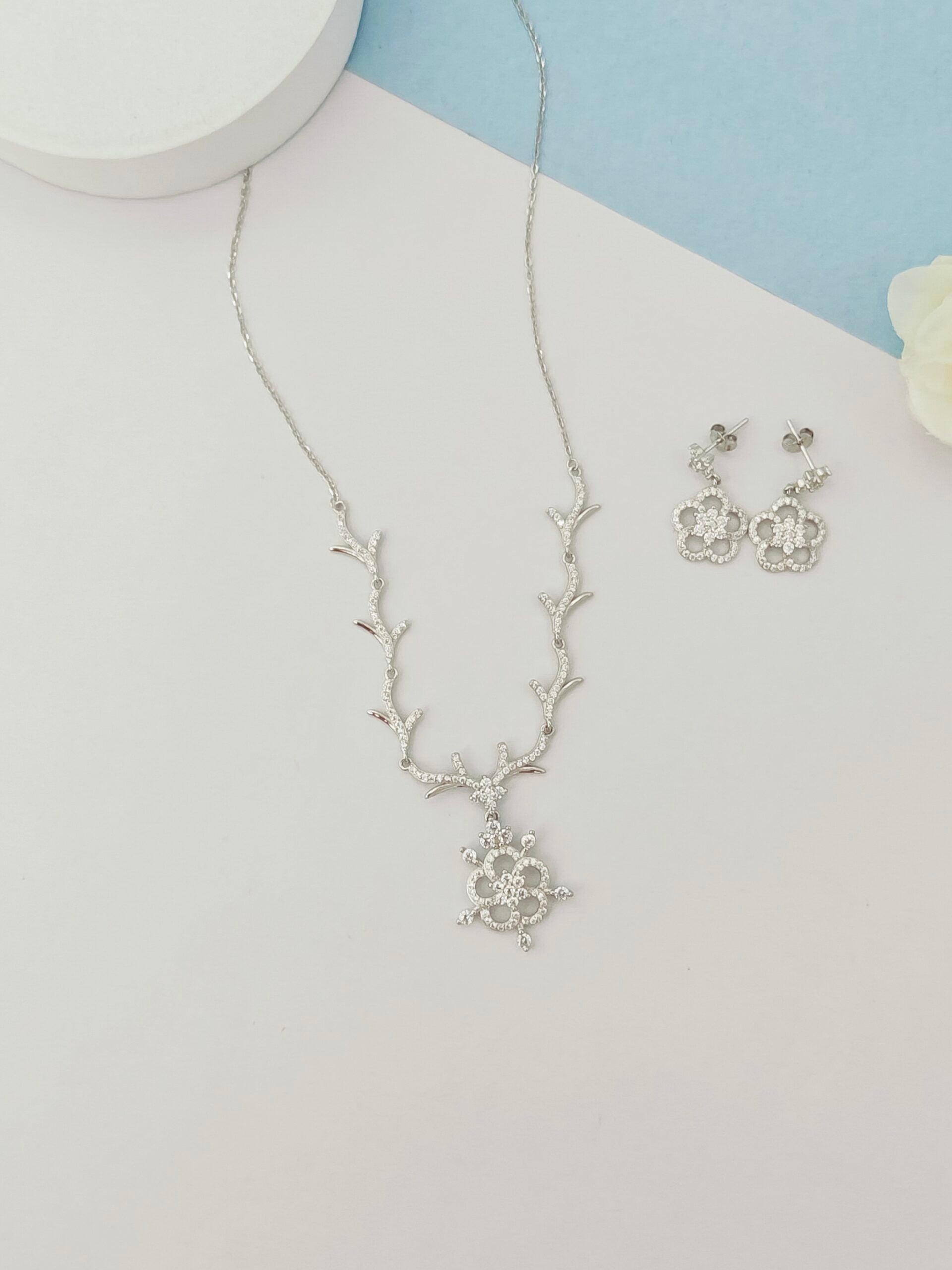 Silver necklace and earrings on a light gray background