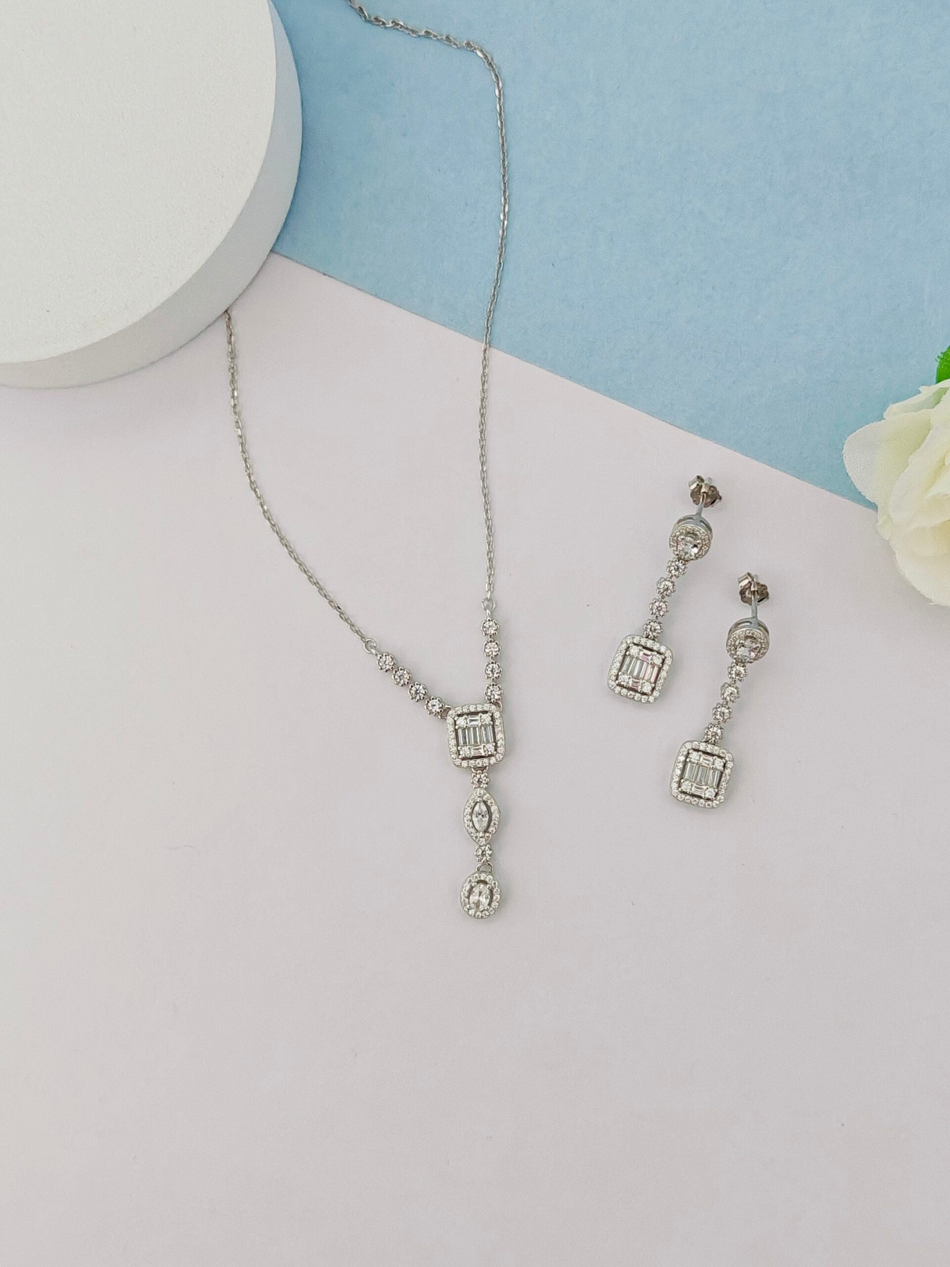 Silver necklace and earrings on a light gray surface with a blue background