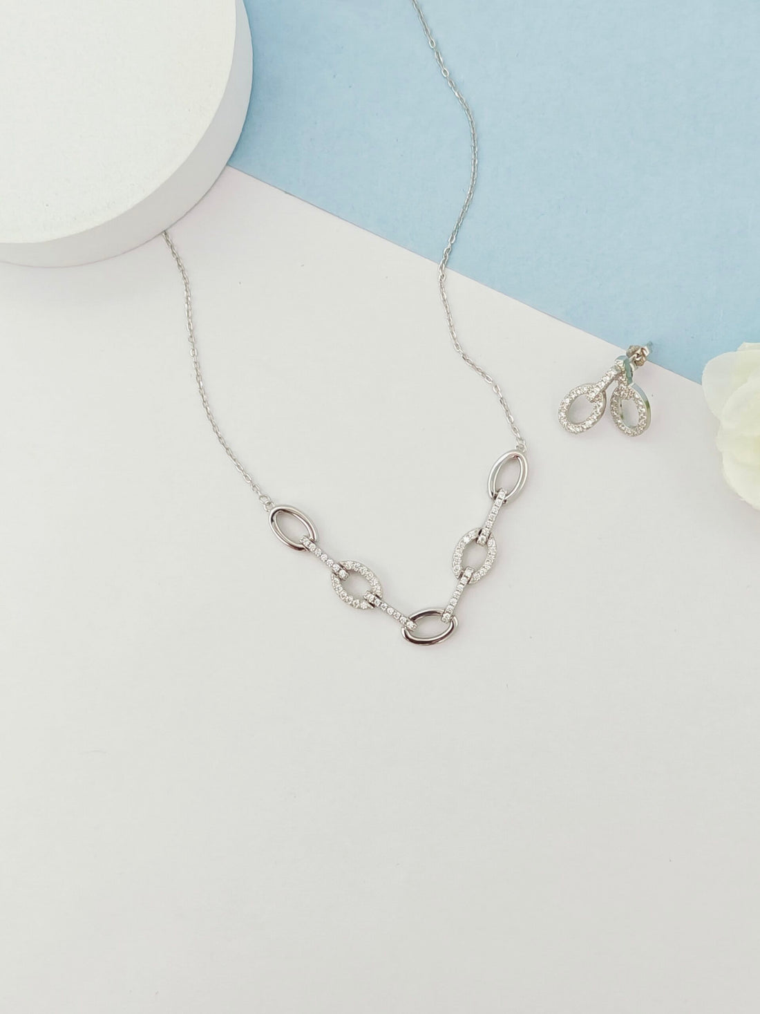 Silver necklace and earrings on a light blue and white background