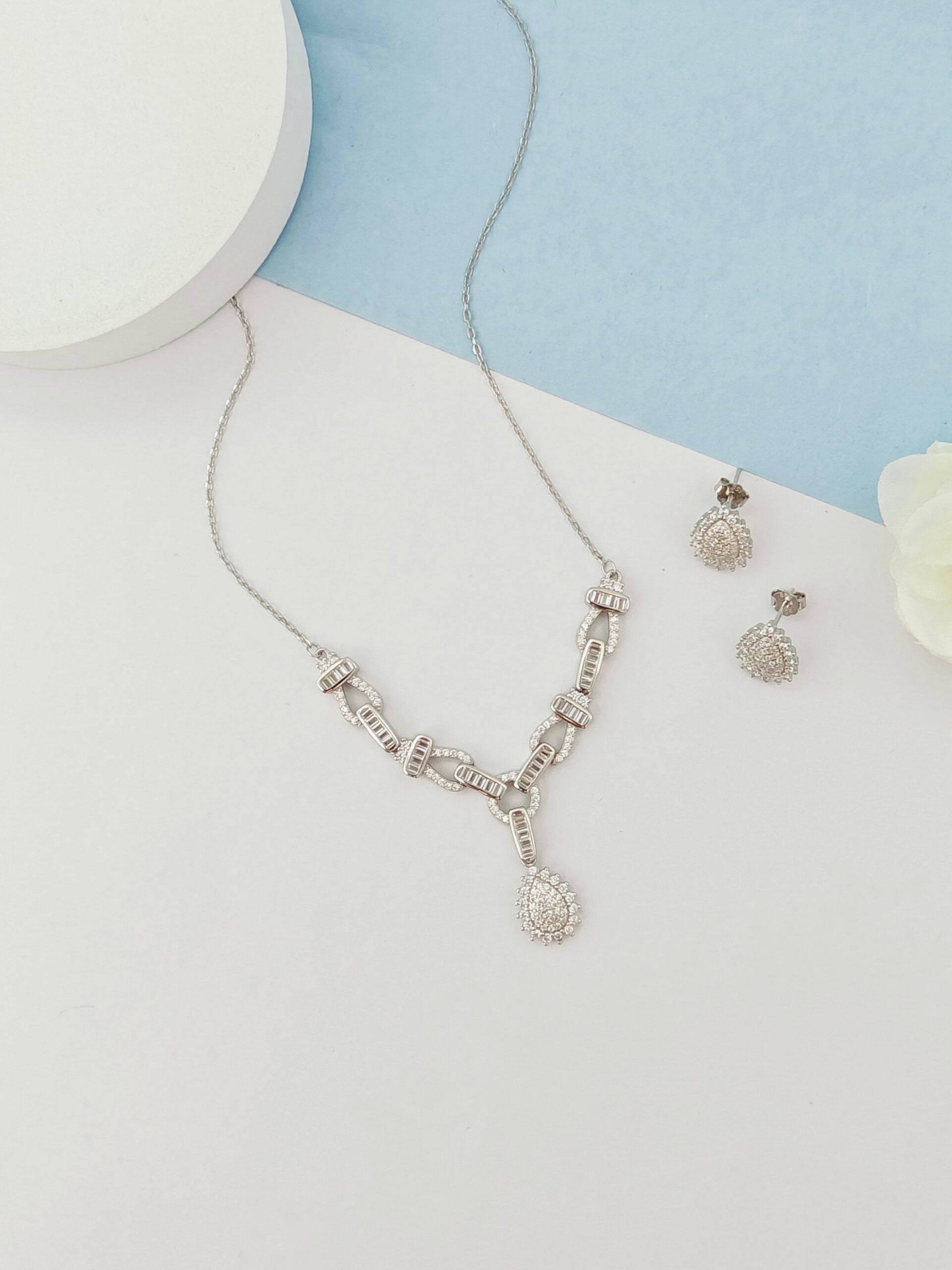 Silver necklace and earrings on a light blue and white background