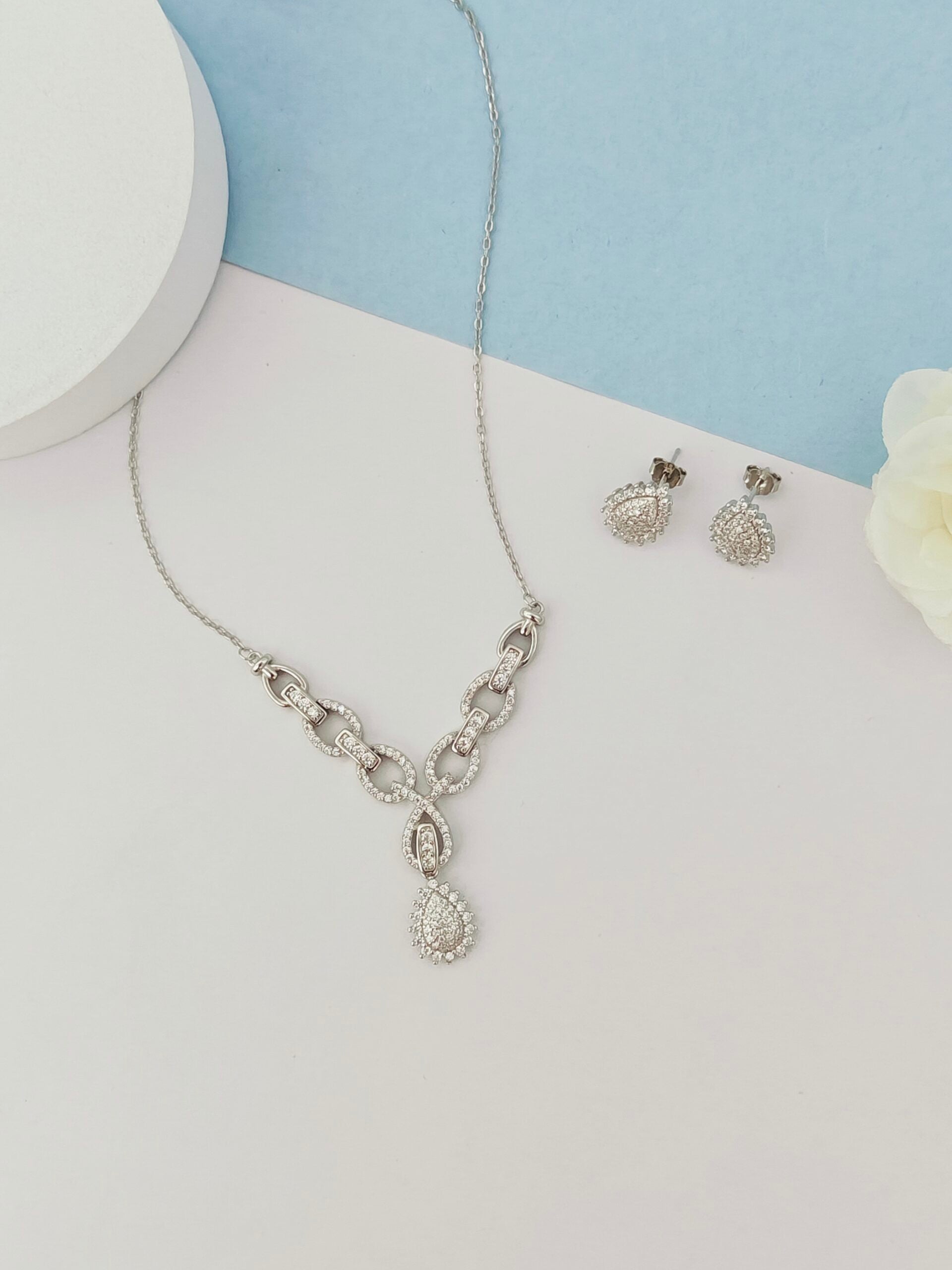 Silver necklace and earrings on a light blue and white background