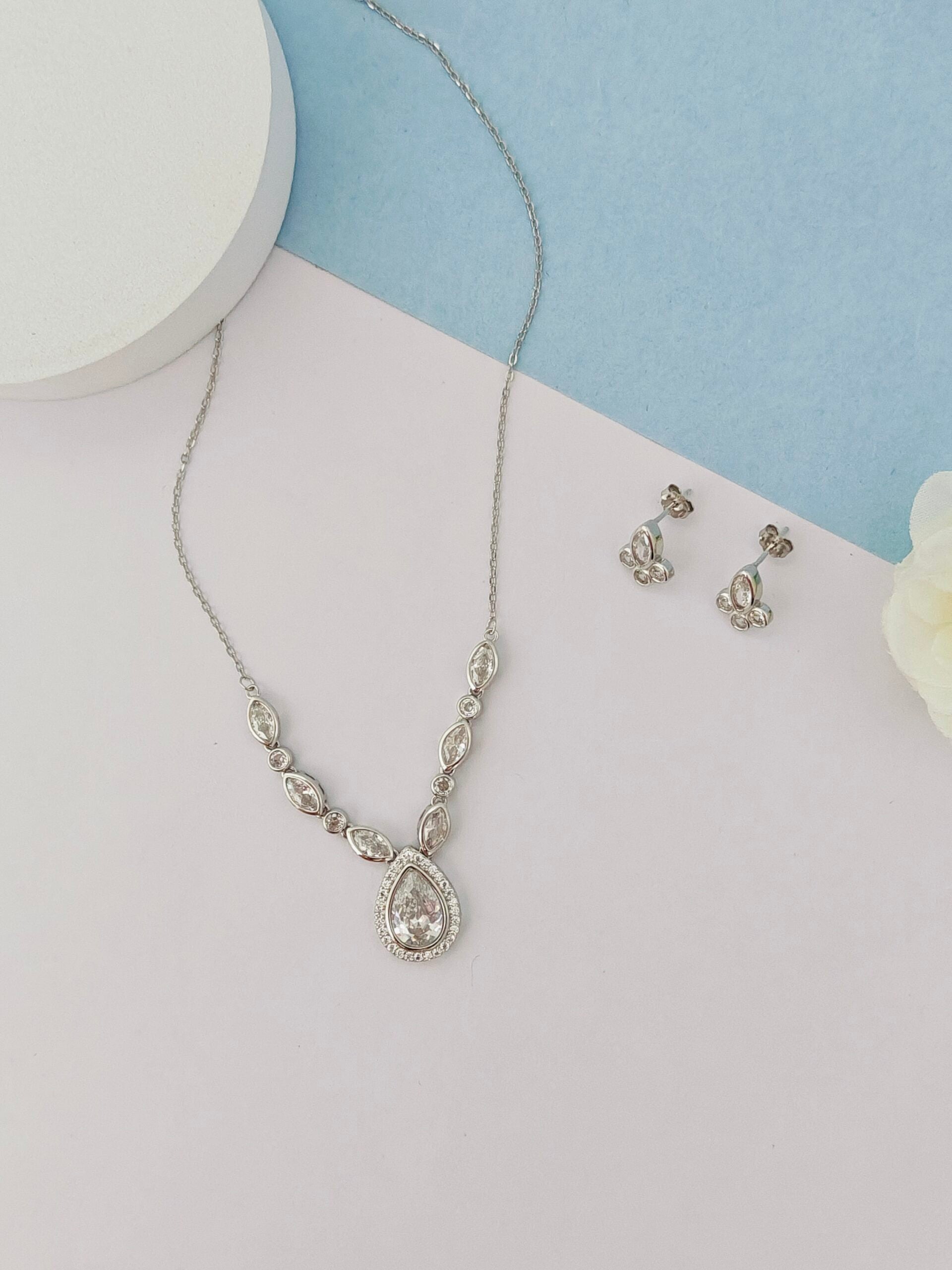 Silver necklace and earrings on a light blue and white background
