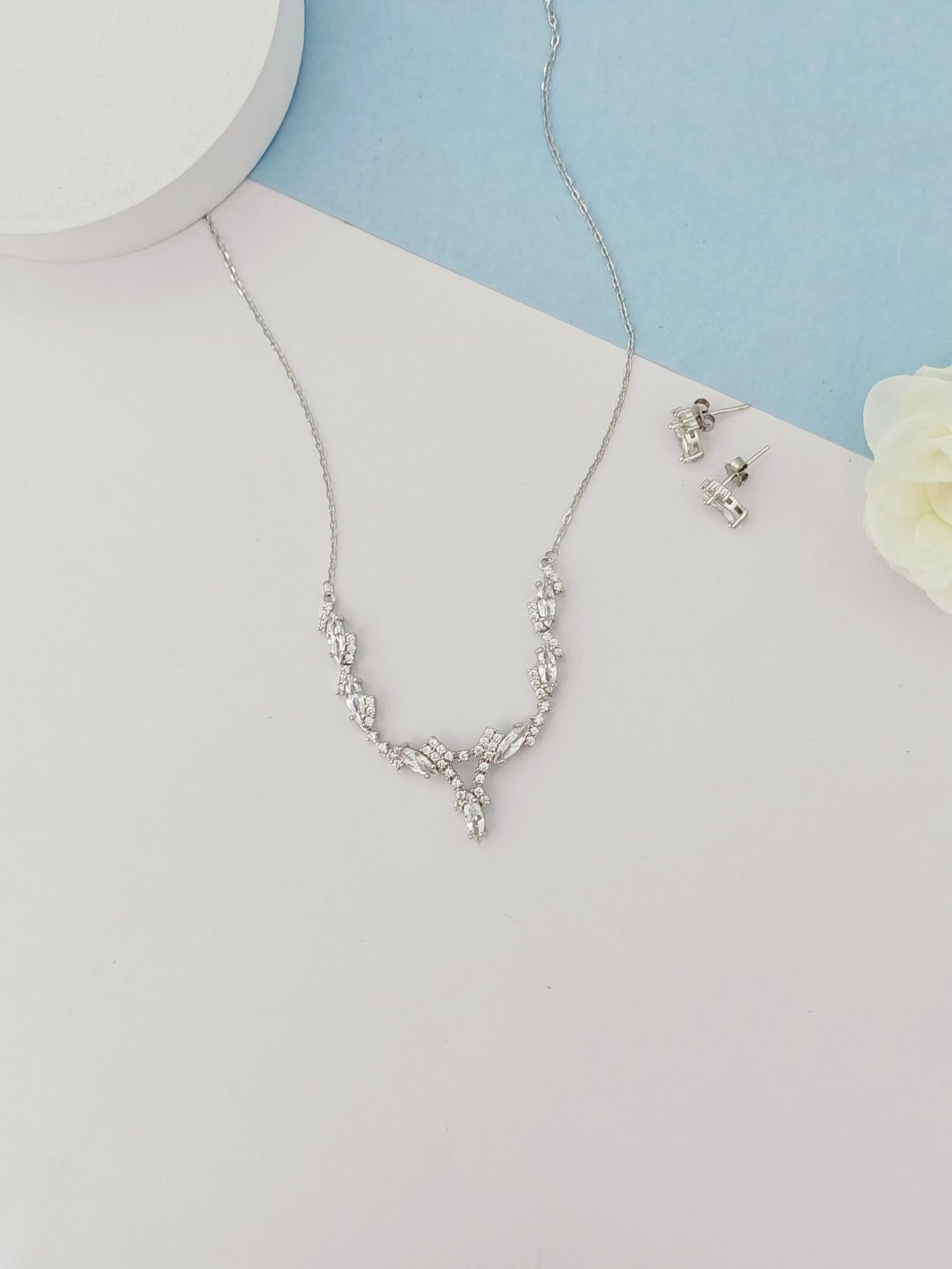 Silver necklace and earrings on a light gray surface with a blue background