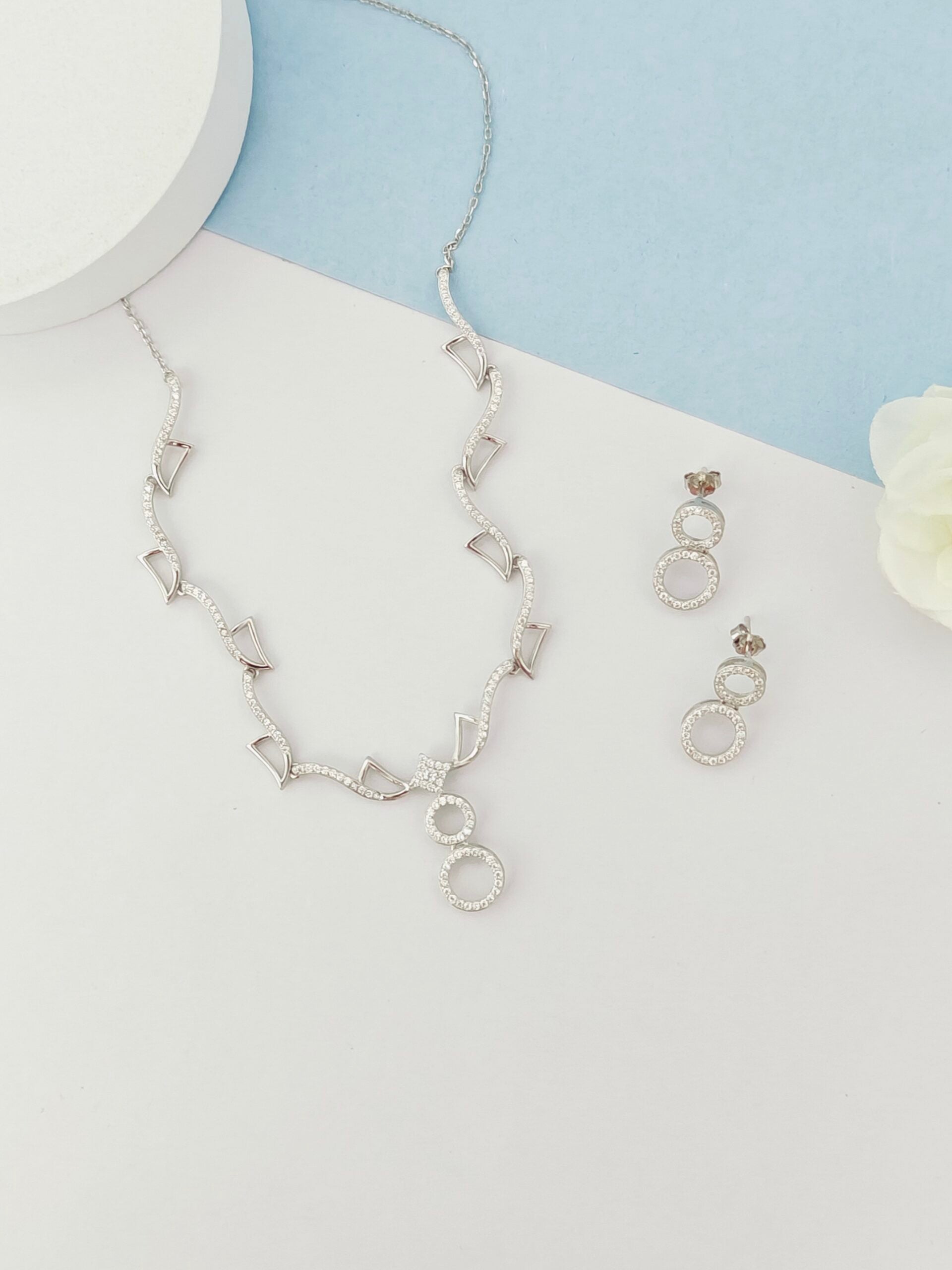 Silver necklace and earrings on a light blue and white background