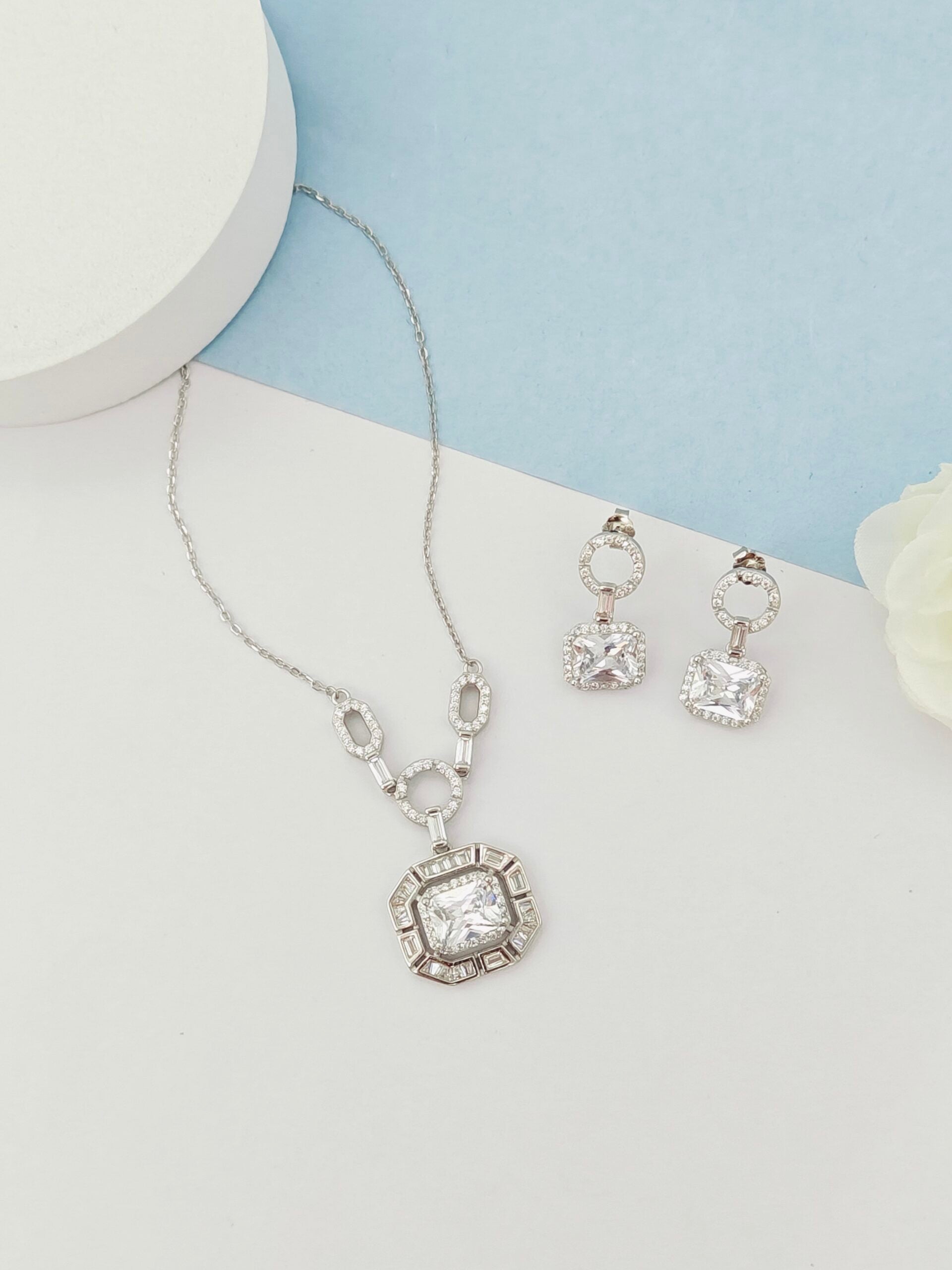 Silver necklace and earrings set on a light blue and white background