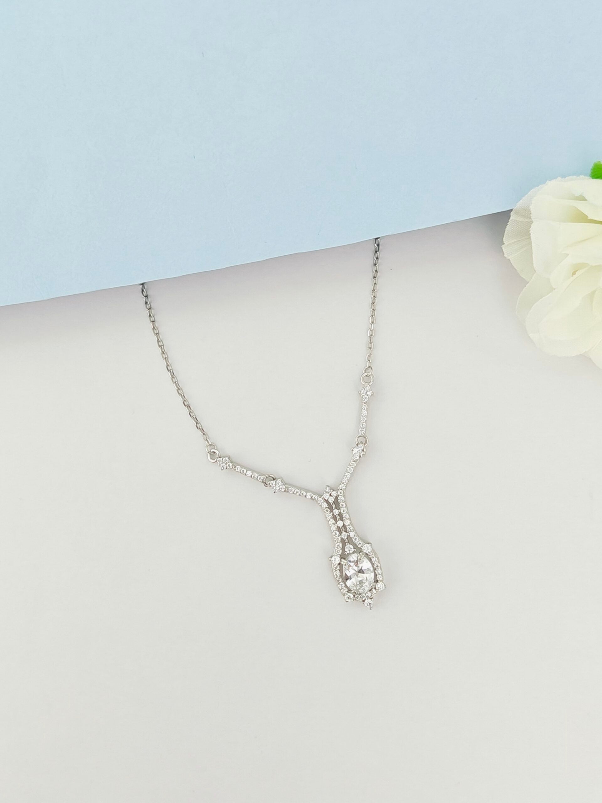 Silver necklace with a teardrop pendant on a mannequin bust against a light blue background.