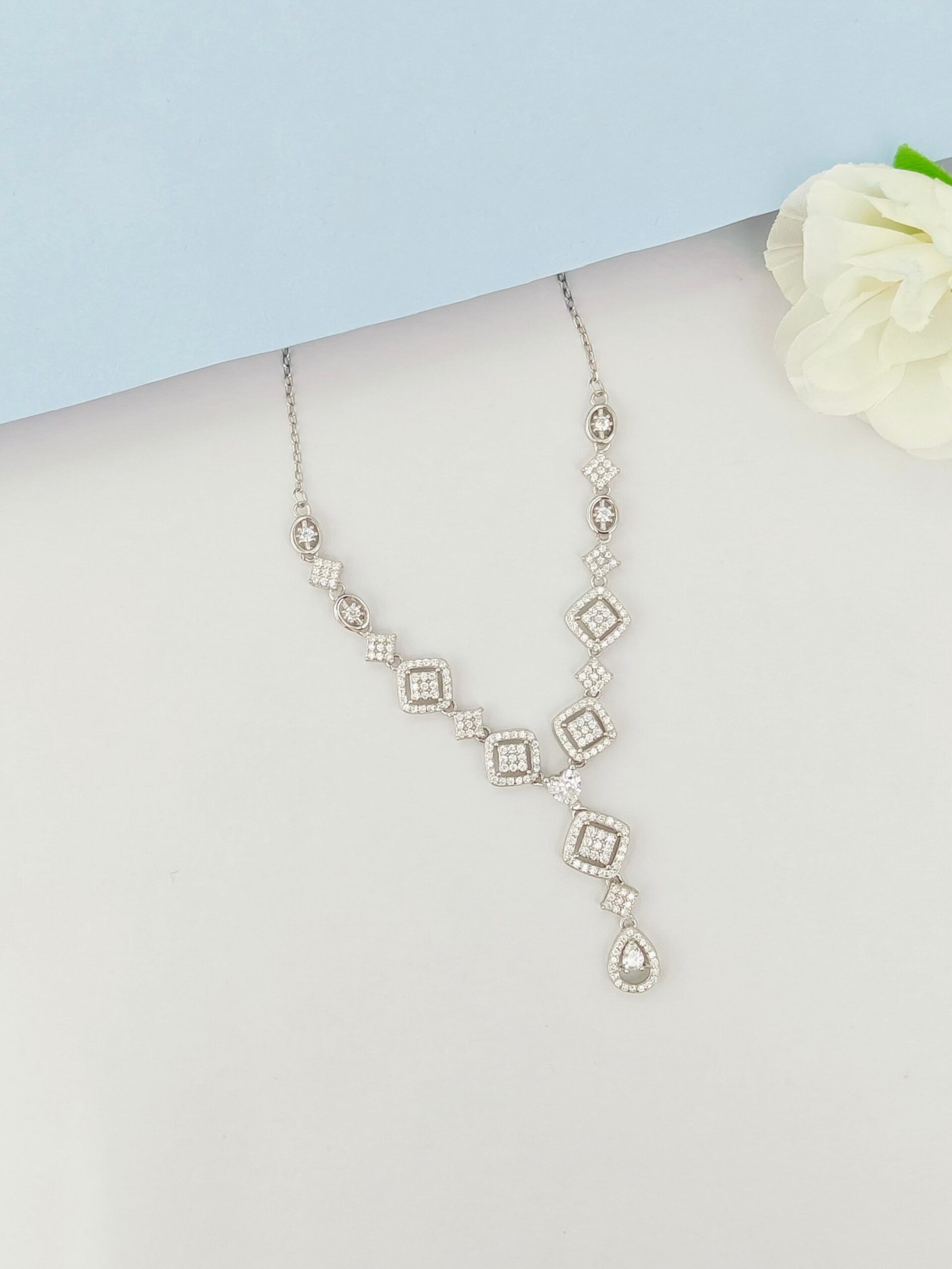 Silver necklace on a mannequin with a white flower background