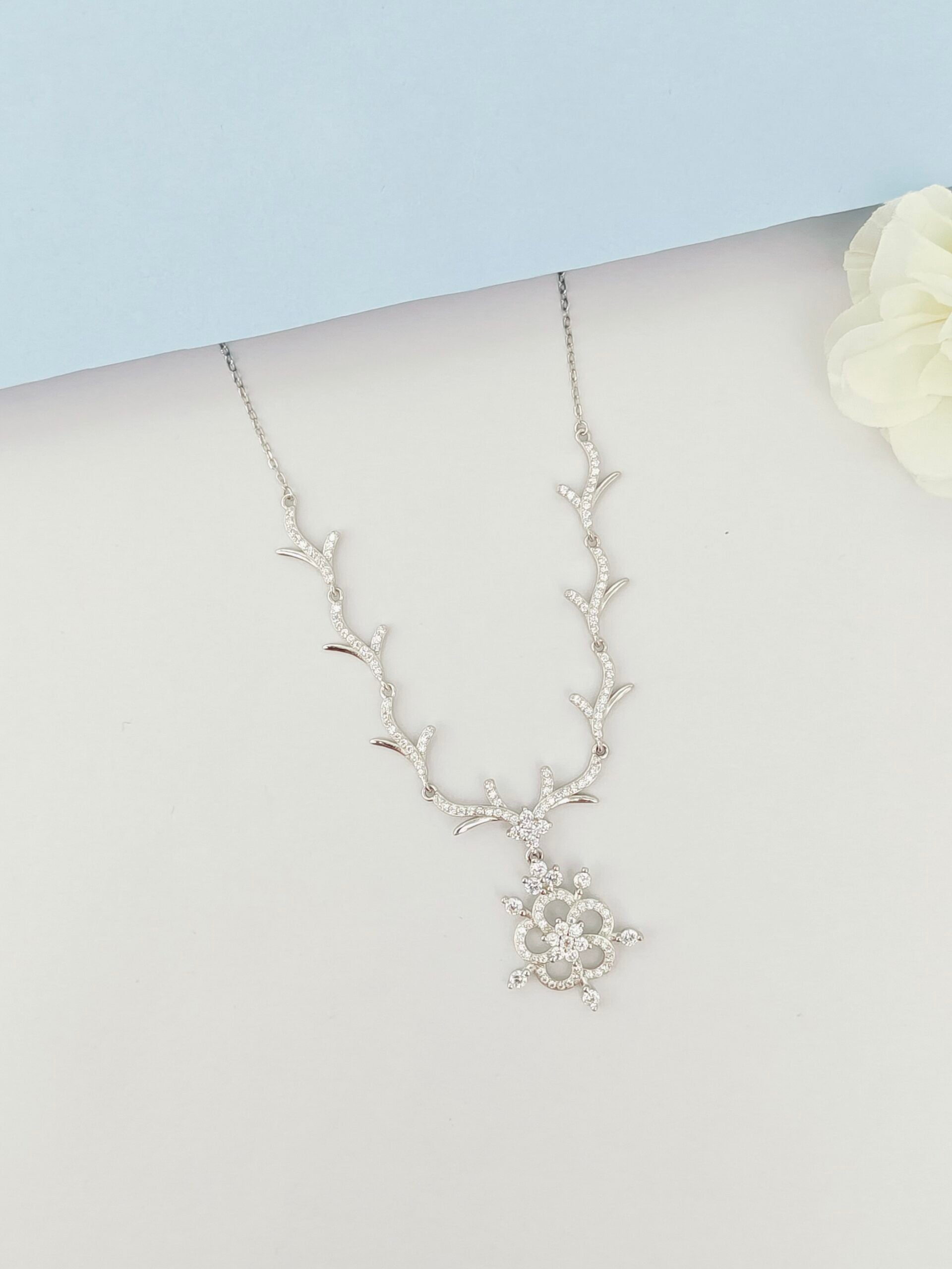 Silver necklace with floral design on a mannequin bust against a light blue background