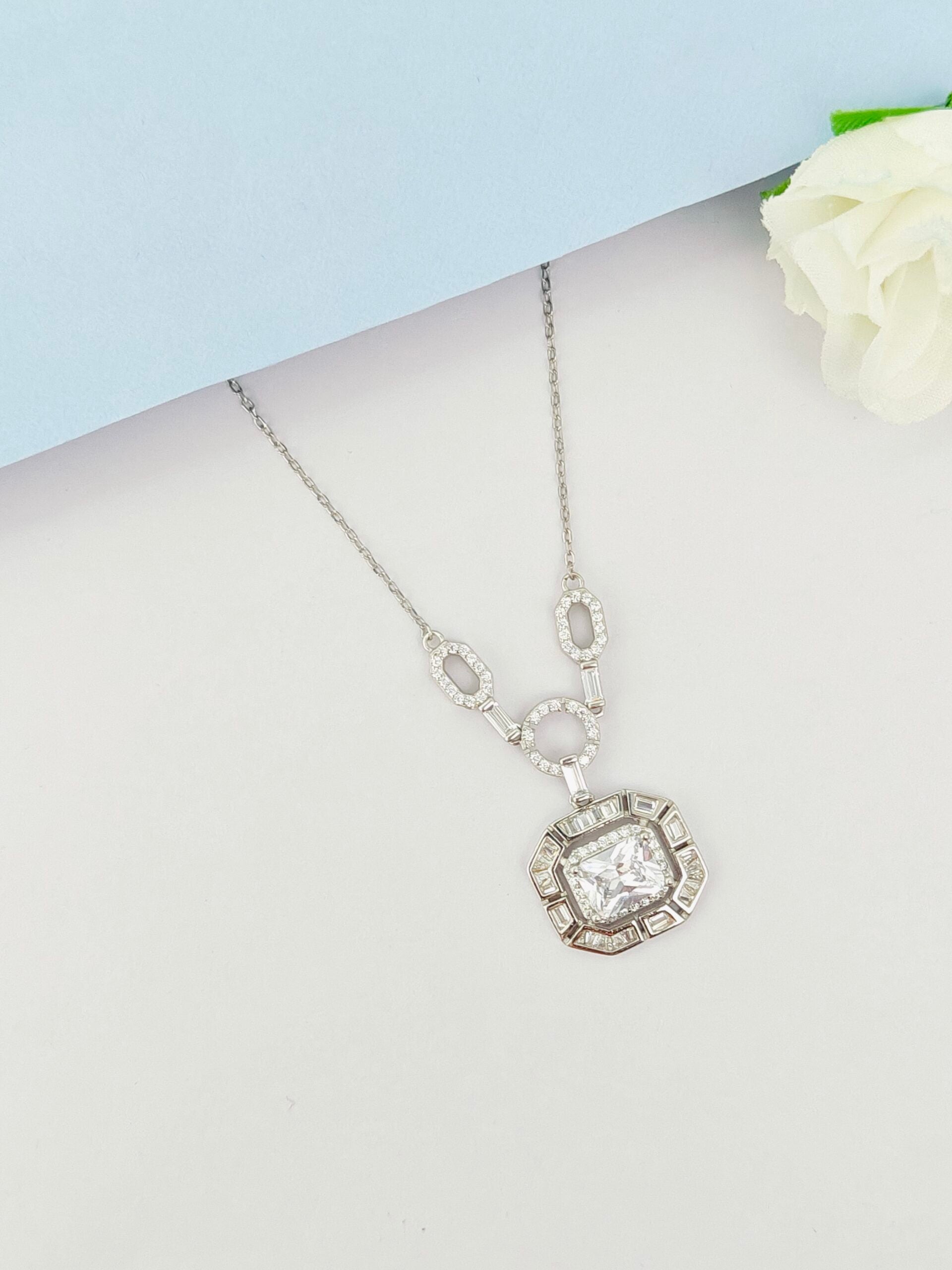 Silver necklace with a pendant on a mannequin bust against a light blue background.