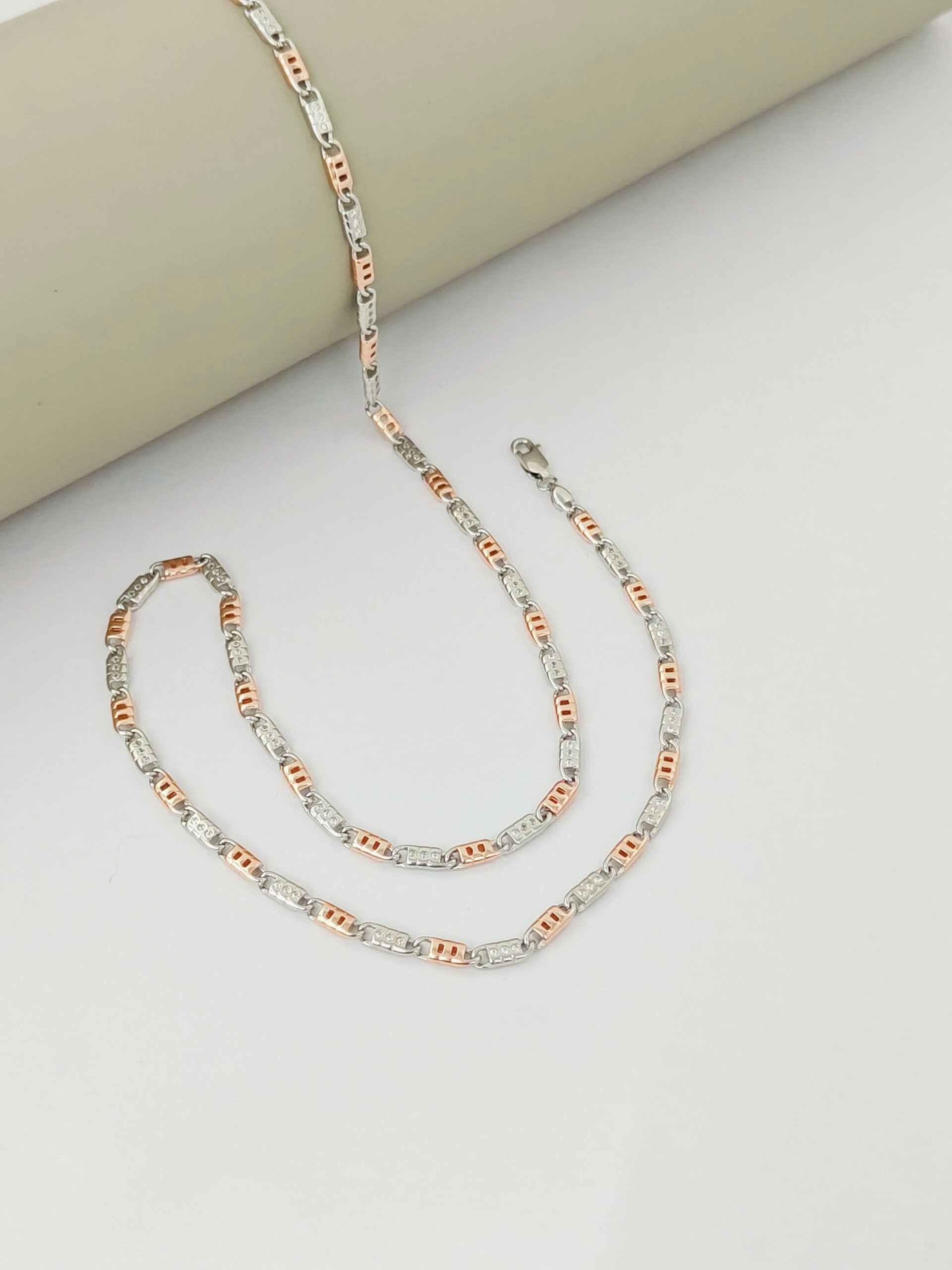 Two gold and silver chain necklaces on a light gray surface.