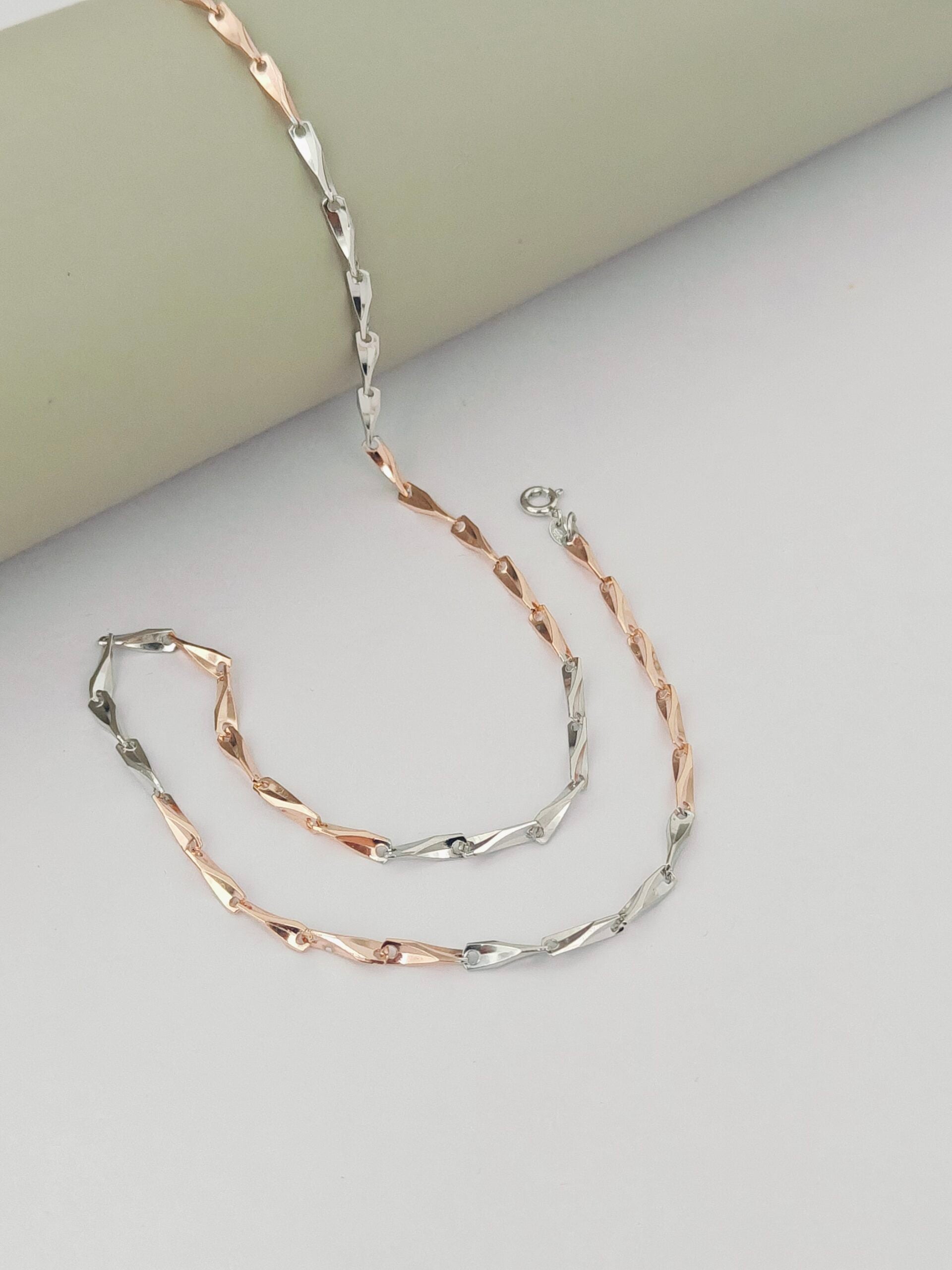 Two rose gold and silver chain necklaces on a light gray surface.
