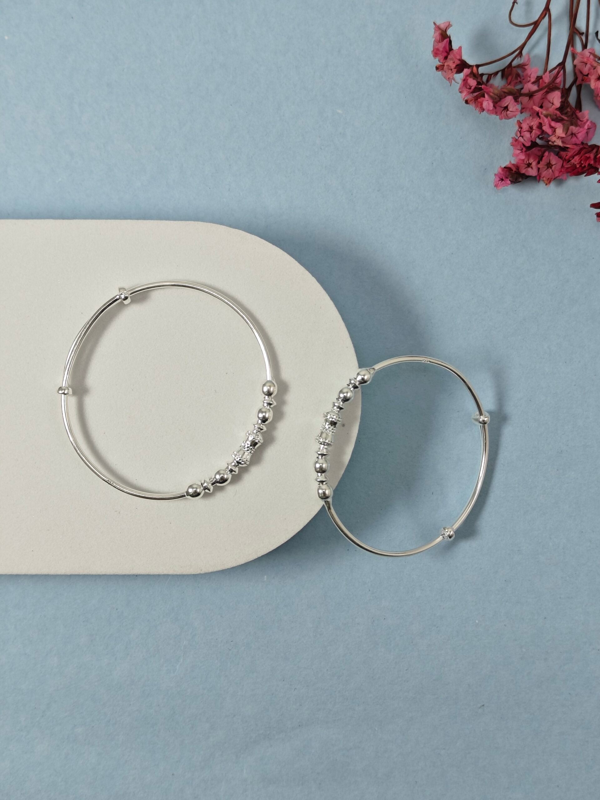 Silver hoop earrings with bead detailing on a light blue background with dried pink flowers.