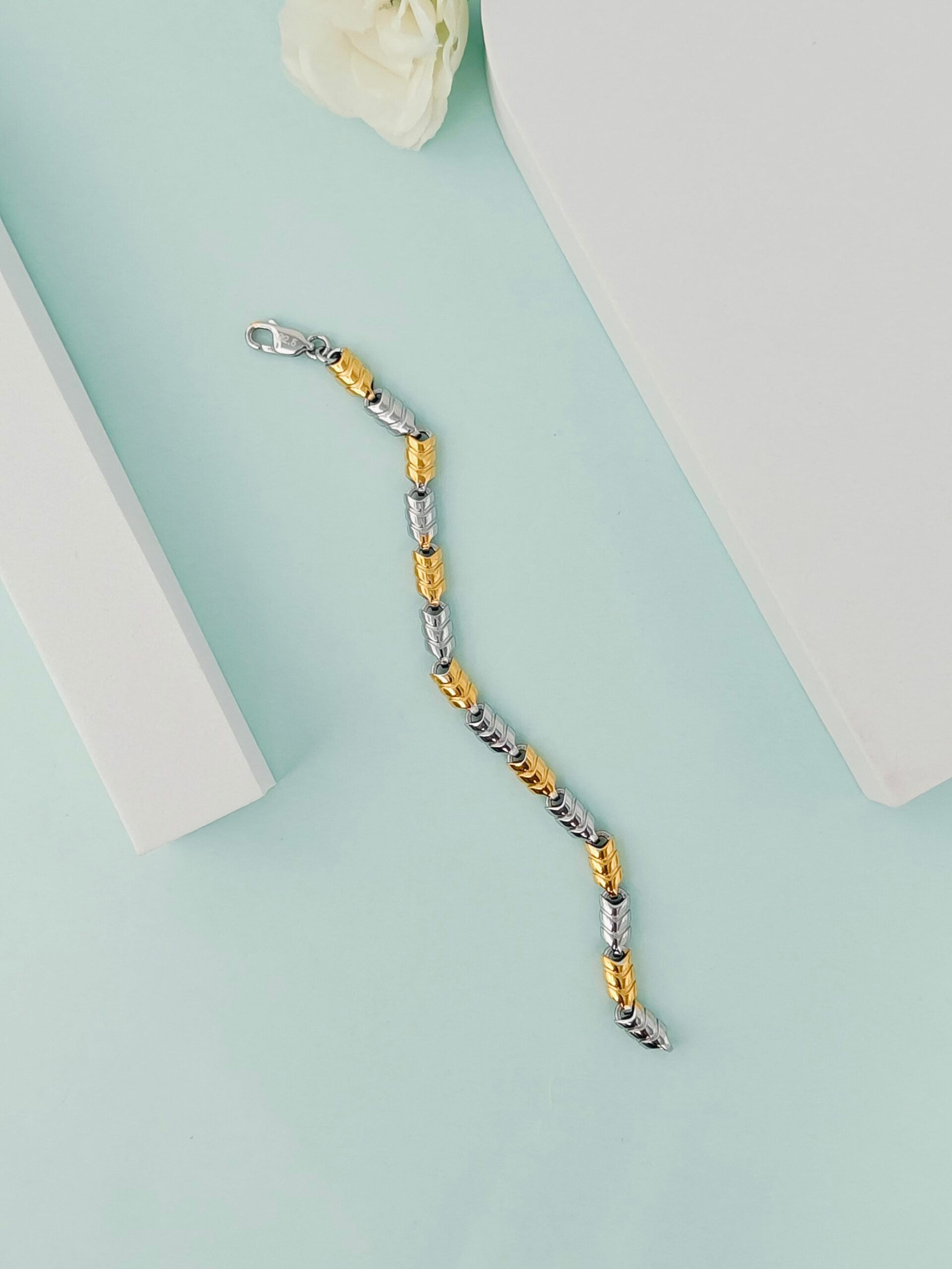 Two-tone bracelet on a light green surface with a white flower in the corner