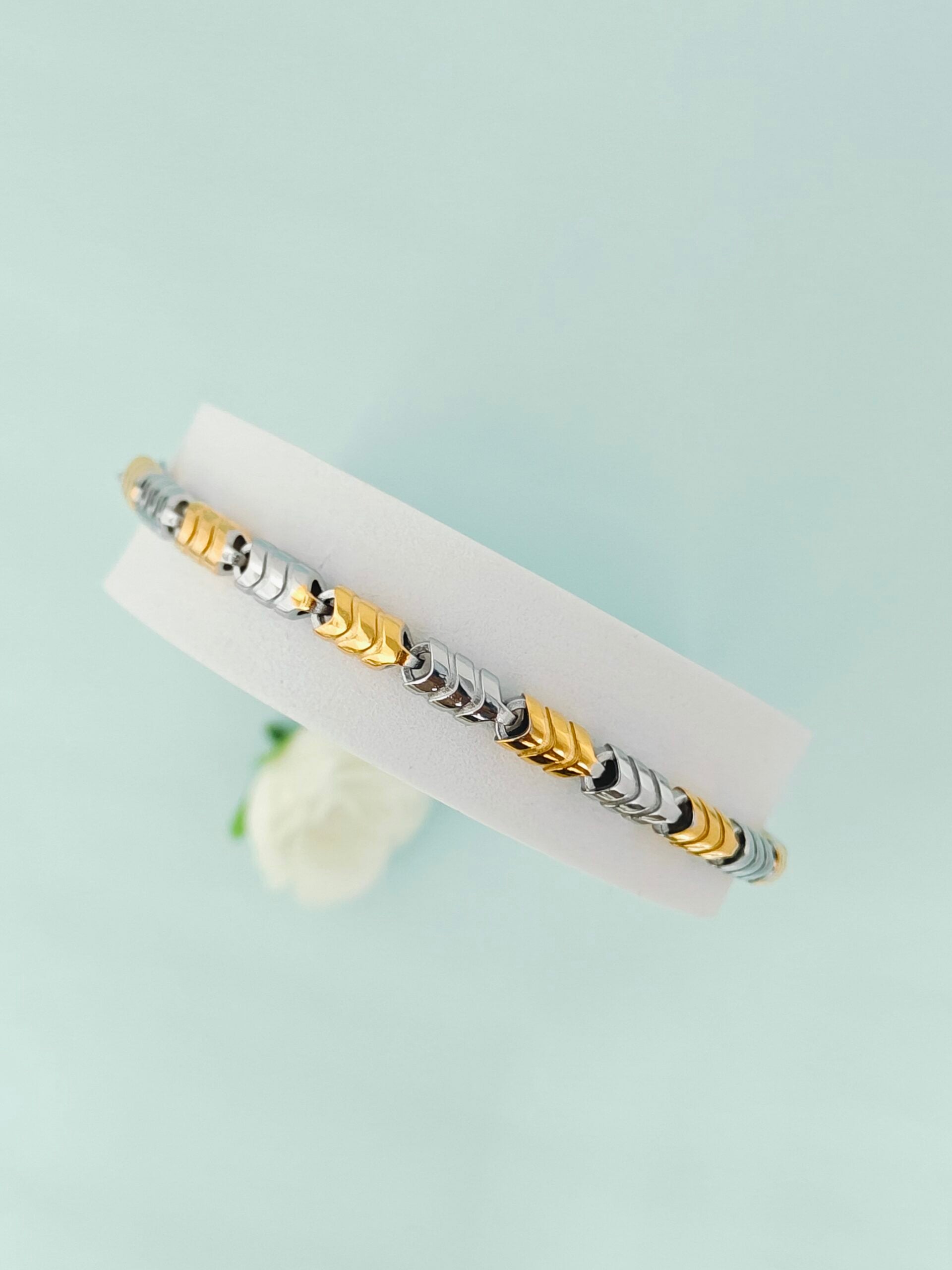 Two gold and silver bracelets on a white stand with a light blue background